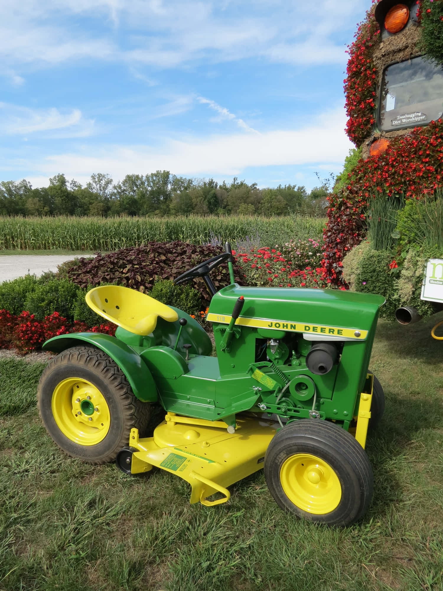 Tractor 桌布 壁紙 — 一台經典綠色和黃色的John Deere拖拉機停在草地上，旁邊有花卉展示，背景是明亮的藍天。
