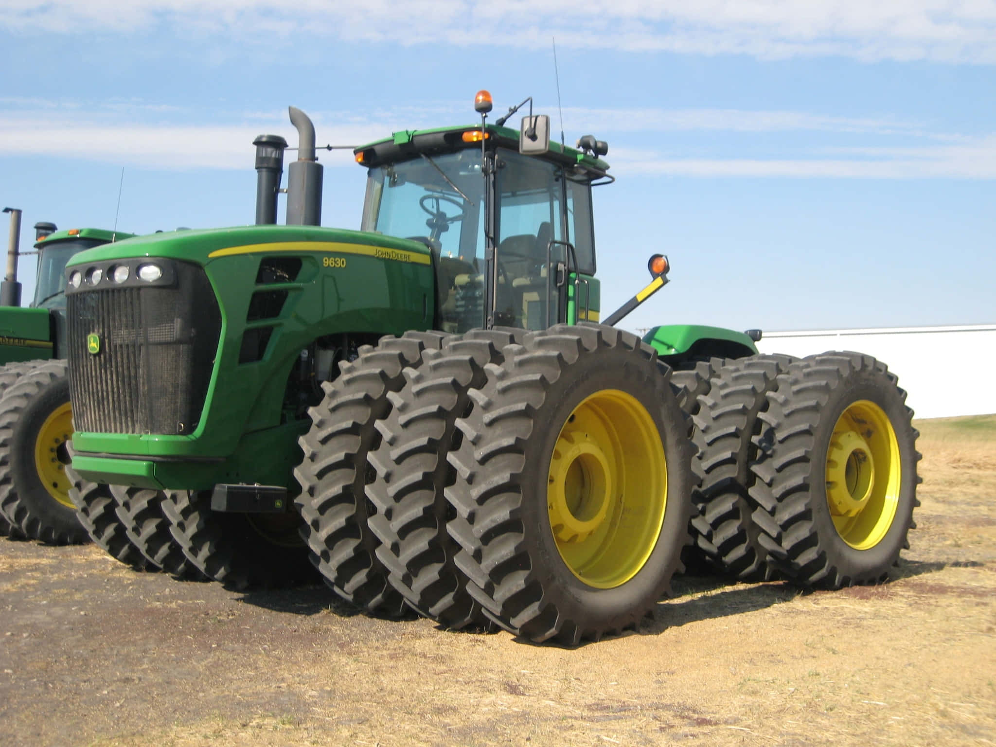 Tractor 桌布 壁紙 — 一台綠色和黃色的John Deere 9630拖拉機配備巨大輪胎，停放在乾燥的土地上，天空清澈湛藍。