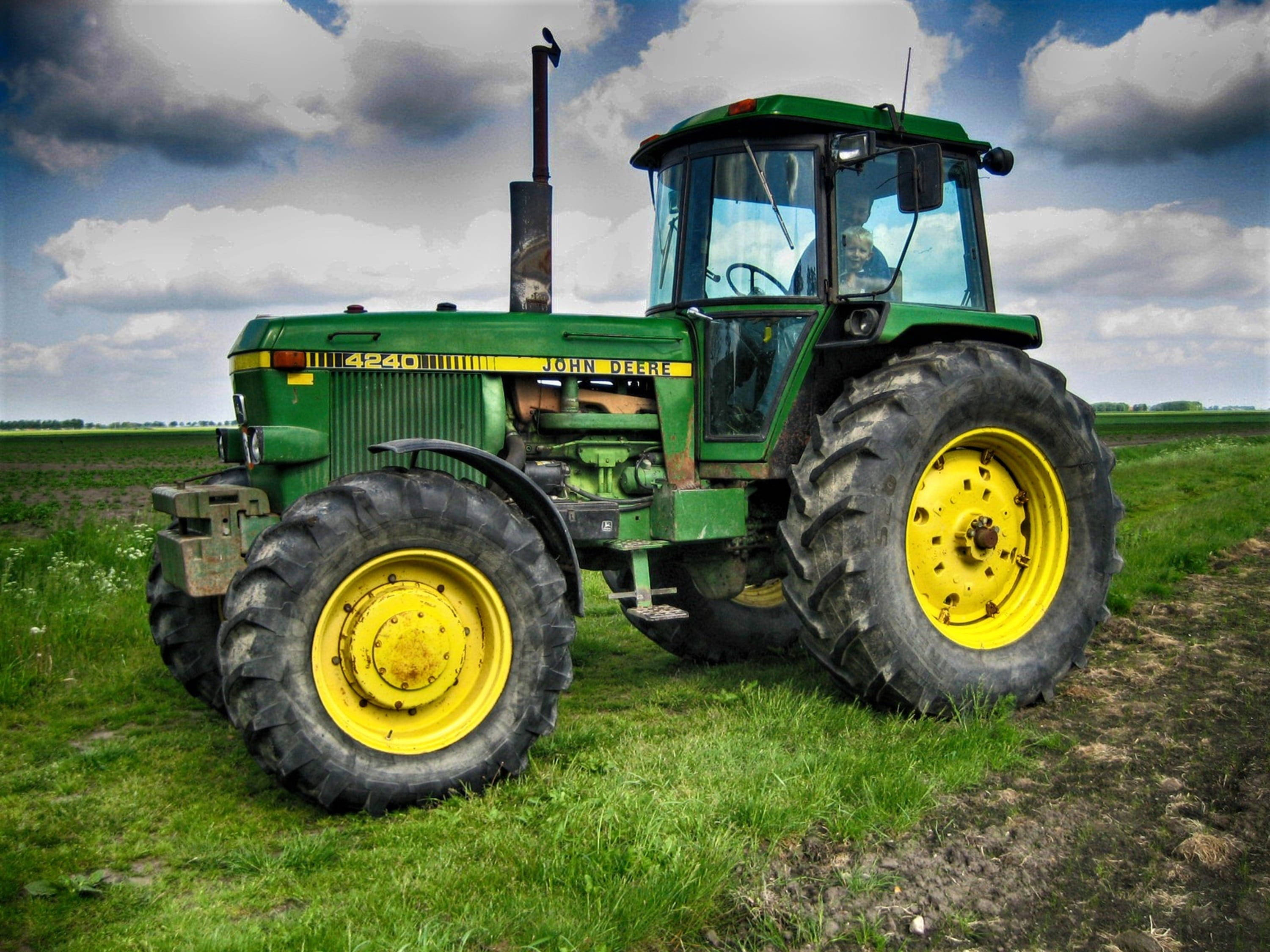 約翰迪爾 桌布 壁紙 — 一台綠色和黃色的John Deere 4240拖拉機停泊在鄉村田野的草地上，天空多雲。