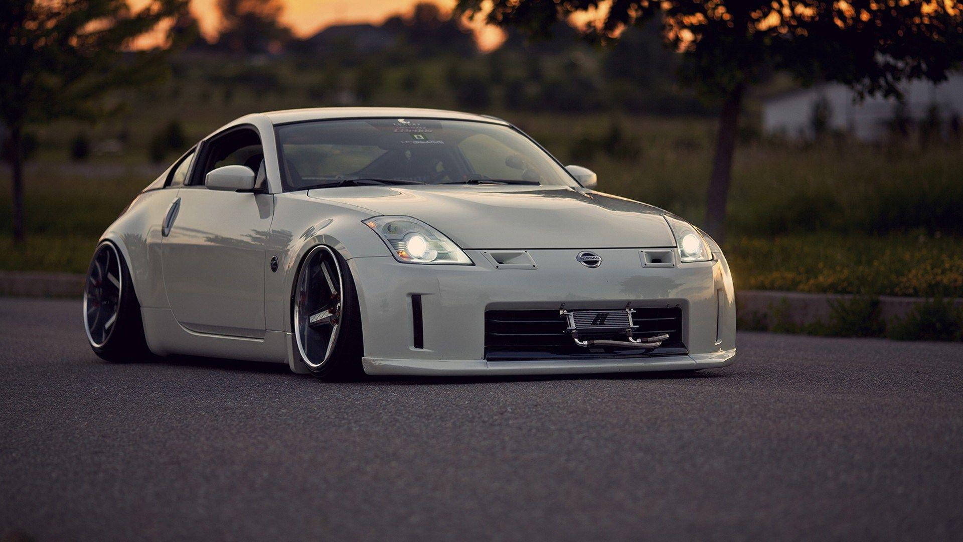 Nissan 350z 桌布 壁紙 — 一台線條流暢的白色日產350Z跑車，配備降低懸吊和發光頭燈，在日落時分停泊在柏油路上。