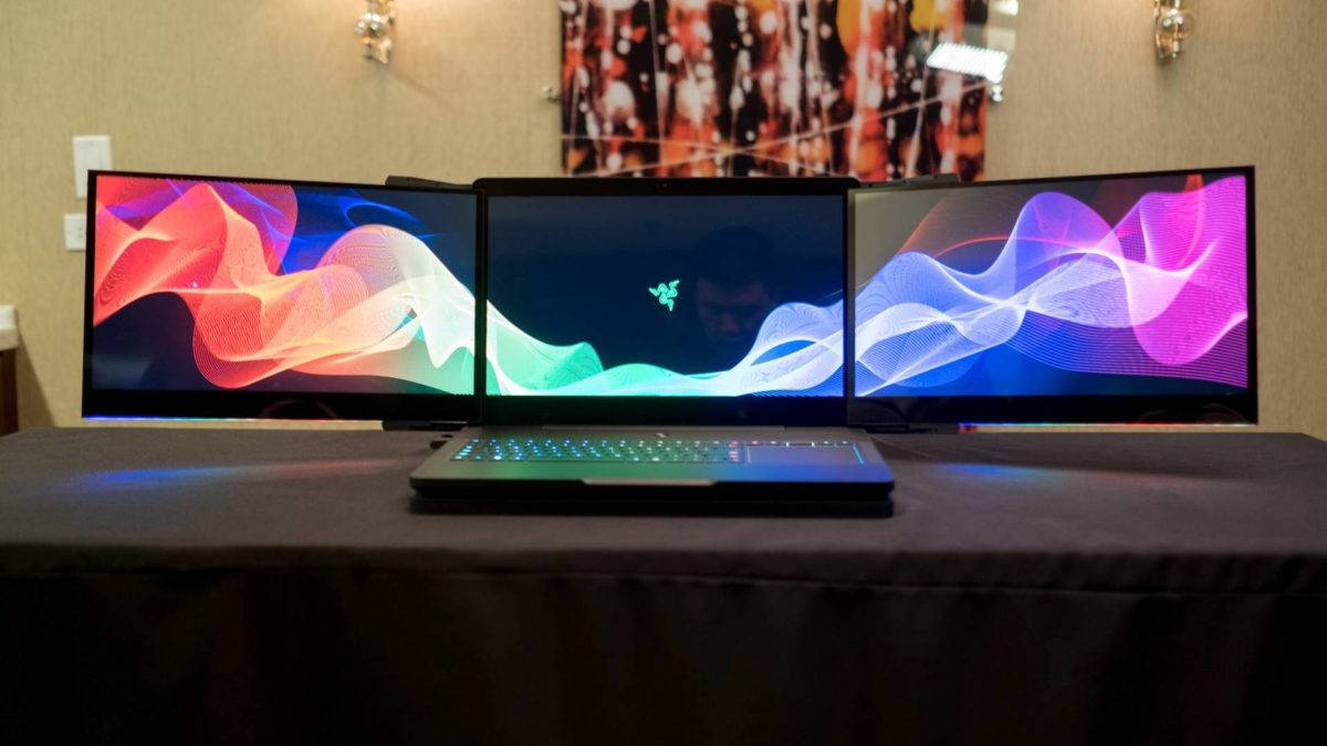 4K 桌布 壁紙 — 一台纖薄筆記型電腦放在深色桌子中央，兩側有兩部曲面顯示器顯示充滿活力的抽象波浪桌布。