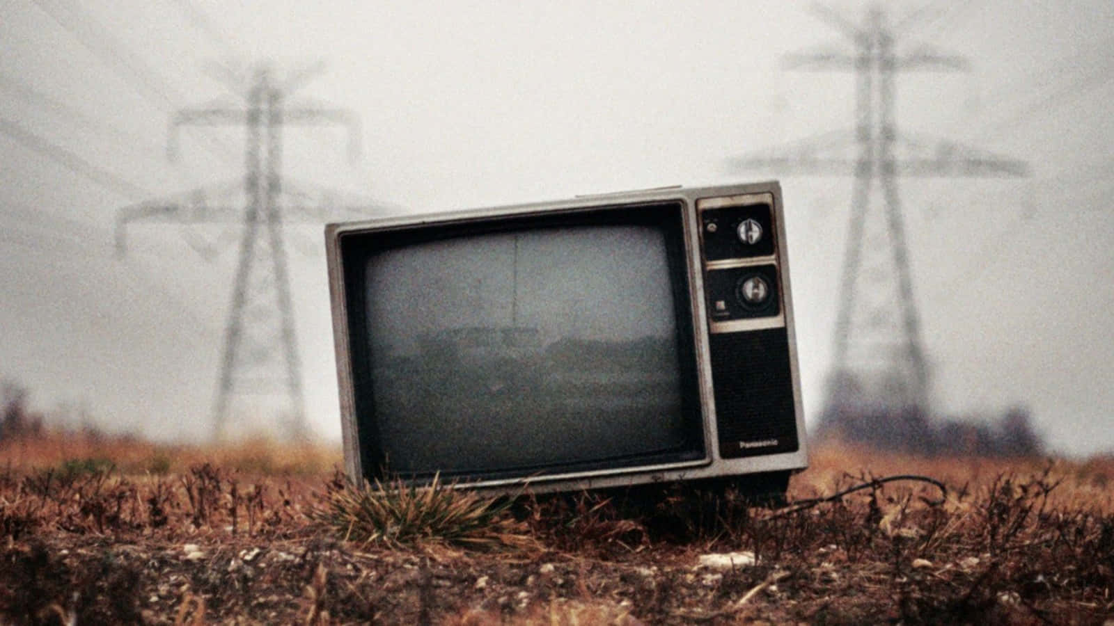 tv 桌布 壁紙 — 一台舊Panasonic電視被遺棄在乾燥的田野中，霧氣籠罩的背景裡電線杆聳立。