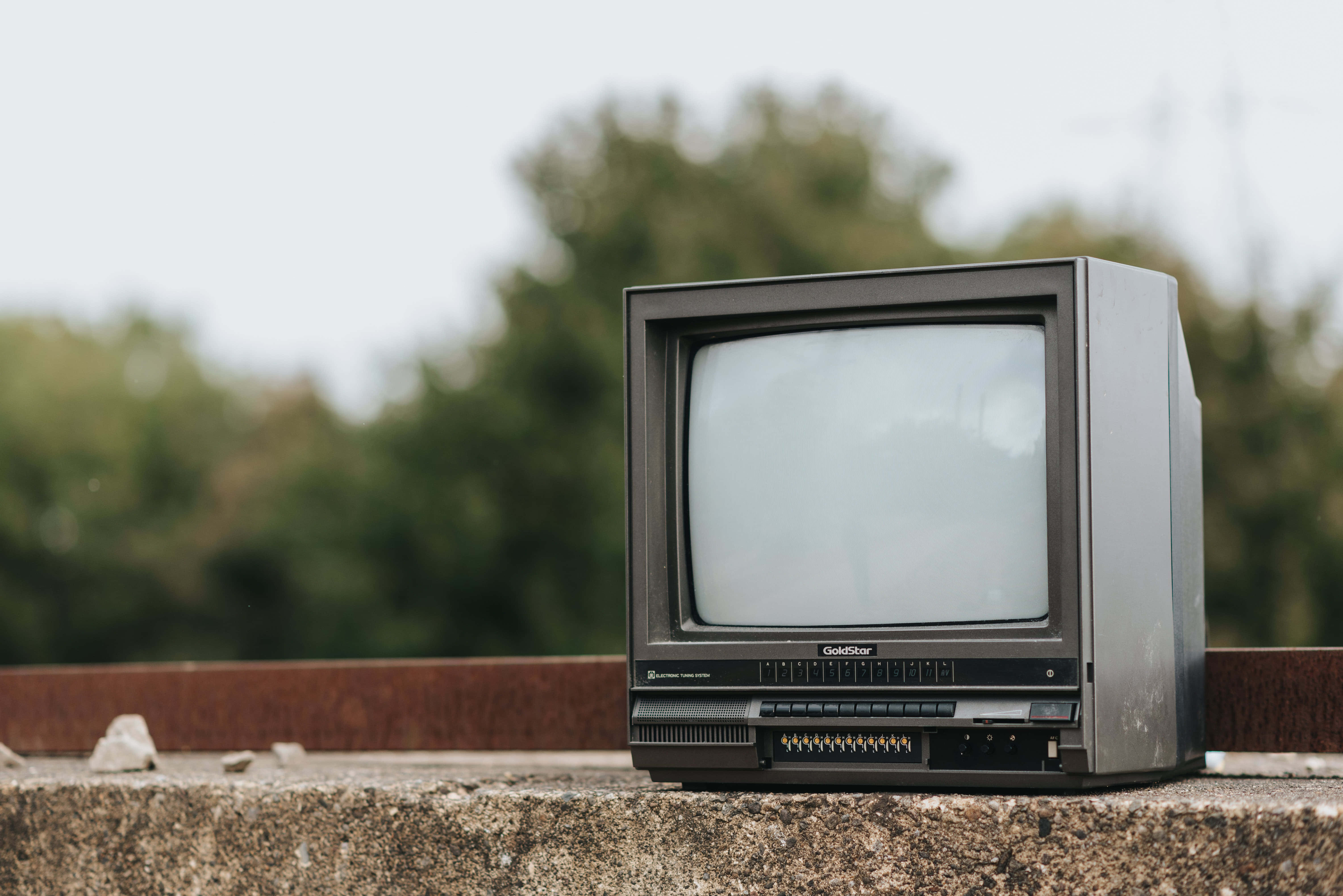 television 桌布 壁紙 — 一台舊式笨重的CRT電視被遺棄在混凝土簷上，背景有模糊的綠色樹木。