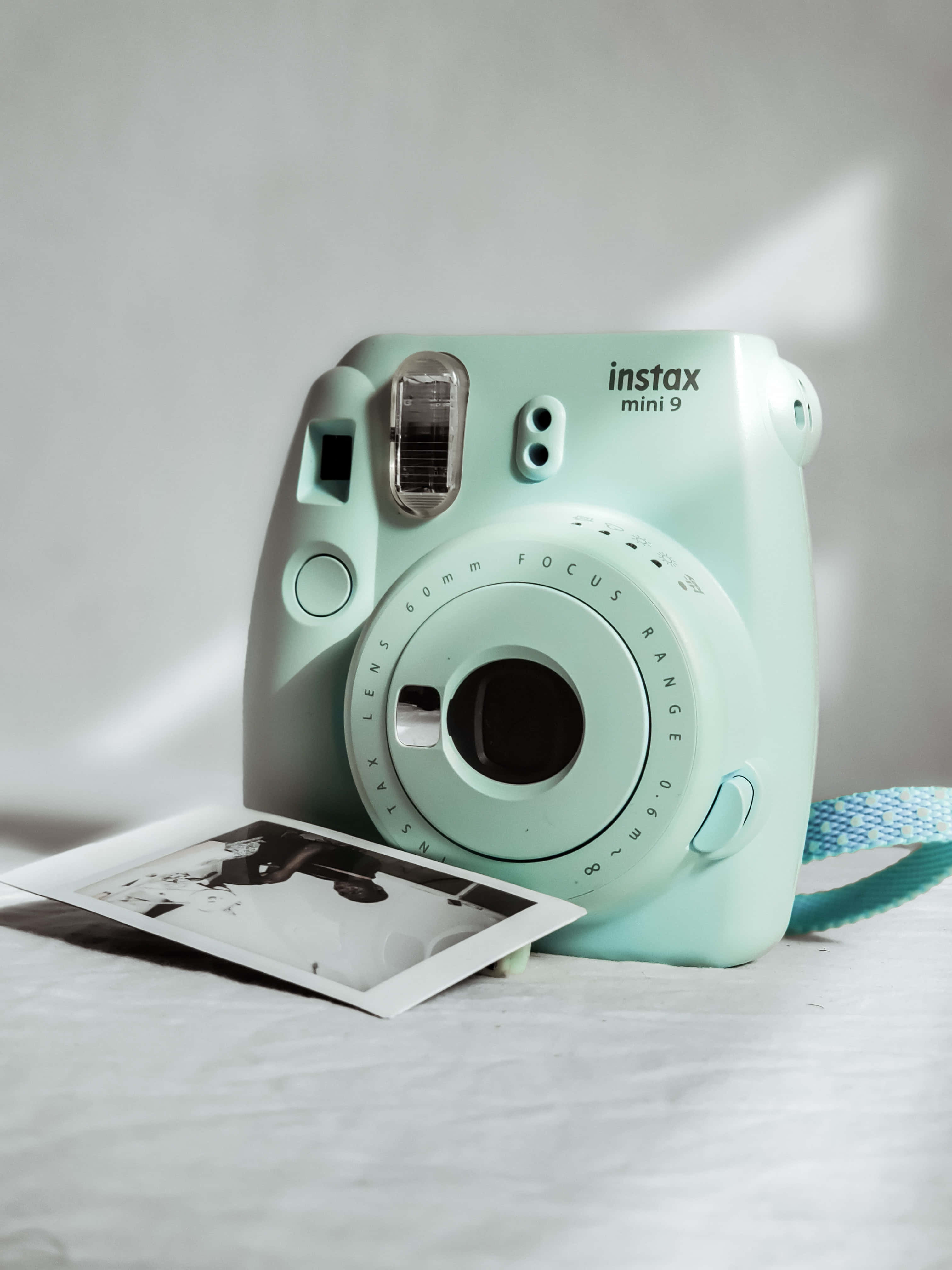 Polaroid Camera 桌布 壁紙 — 一台薄荷綠色的Instax Mini 9相機放在白色表面上，一張列印出來的照片從其插槽中露出。