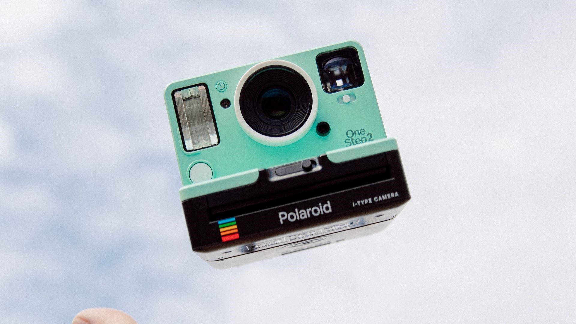 拍立得 桌布 壁紙 — 一台薄荷綠色的Polaroid OneStep2相機漂浮在柔和的雲天中，底部幾乎看不見一根手指。