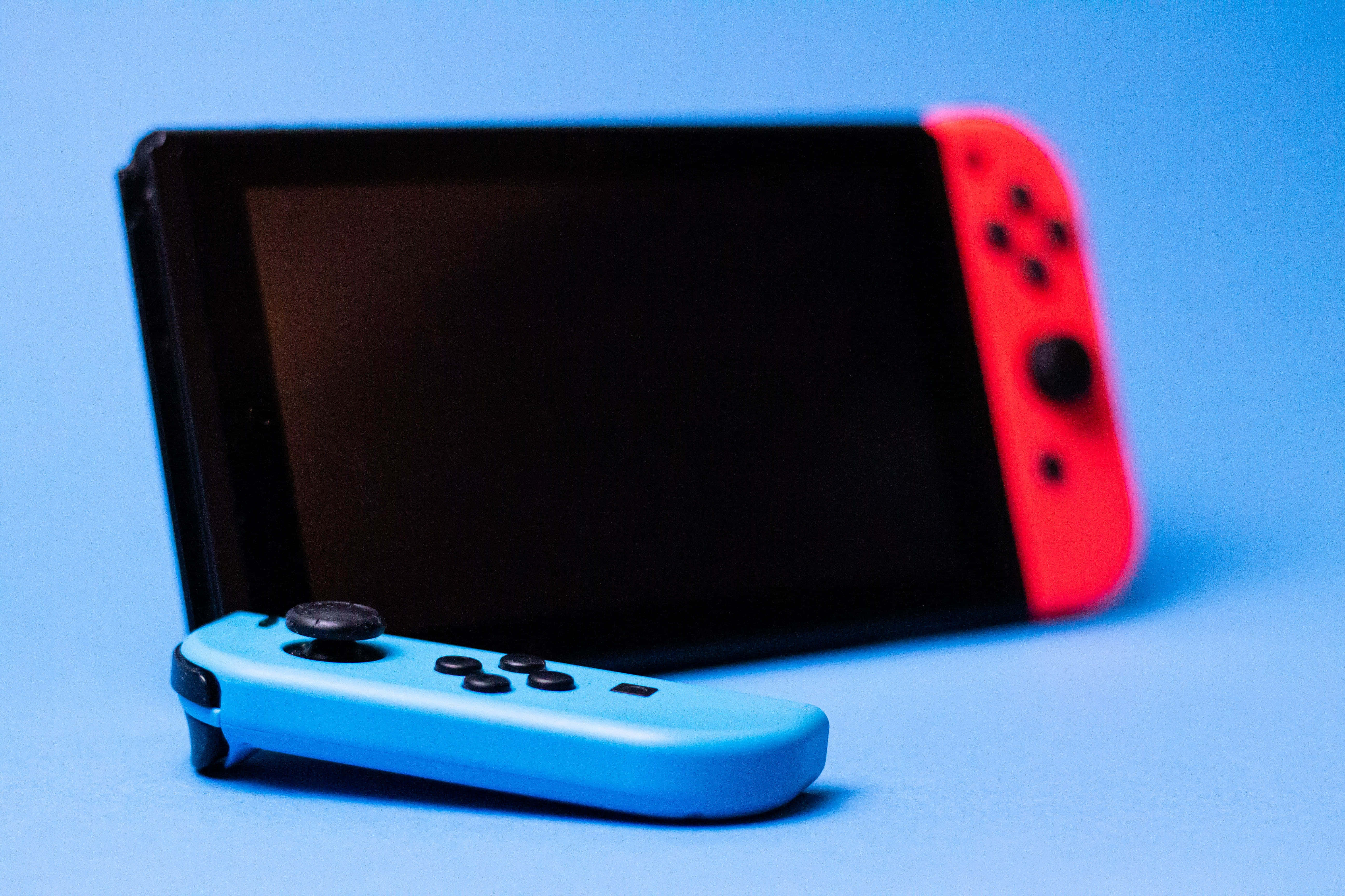 Gaming Consoles 桌布 壁紙 — 一台藍色和紅色的Nintendo Switch主機，帶有分離式控制器，放置在純藍色背景上。