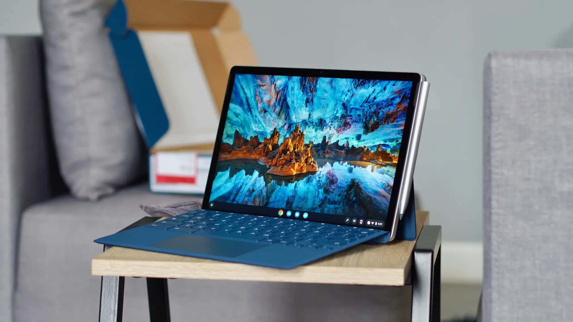 Chromebook 桌布 壁紙 — 一台藍色筆記型電腦在木製邊桌上顯示一個充滿活力的奇幻景觀，發光的橙色岩石形態襯托著旋轉的藍色天空。