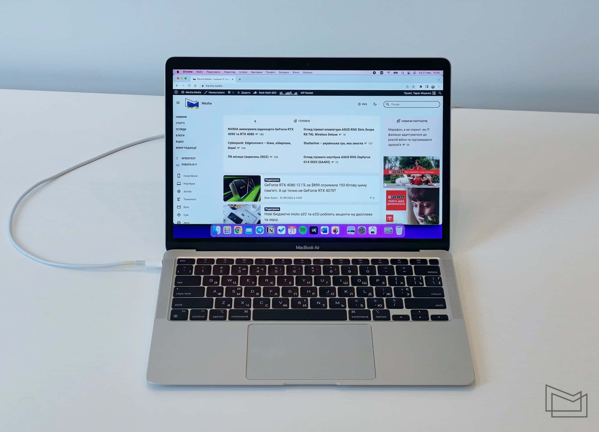 MacBook 動態圖片 桌布 壁紙 — 一台銀色 MacBook Air 筆記型電腦打開放在白色桌子上，顯示一個俄羅斯科技新聞網站，並插著一條電線。