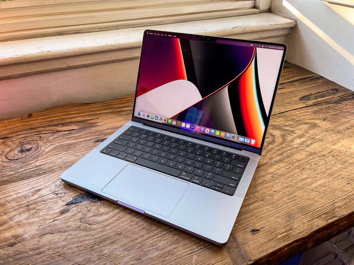 MacBook 動態圖片 桌布 壁紙 — 一台銀色筆記型電腦，顯示色彩繽紛的抽象桌布，打開放在窗邊的鄉村風格木桌上。