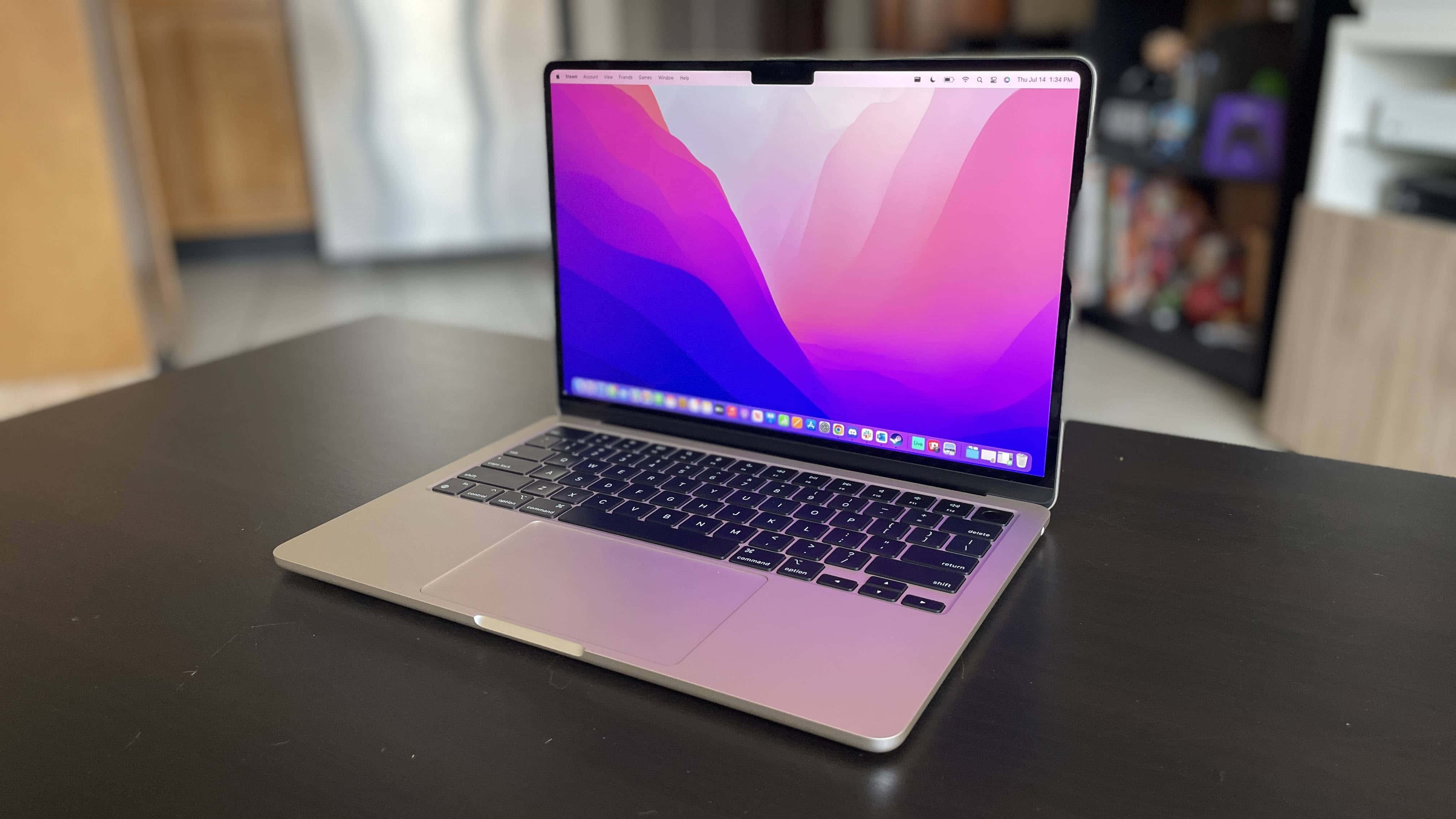 MacBook 動態圖片 桌布 壁紙 — 一台銀色筆記型電腦，顯示著充滿活力的粉紅和紫色抽象桌布，打開放在深色木桌上，房間光線柔和。