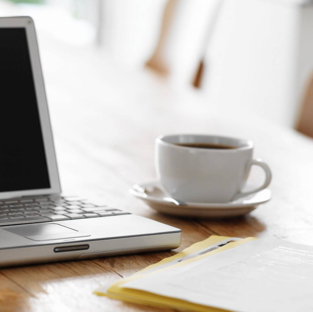 Best Laptop 桌布 壁紙 — 一台銀色筆記型電腦和一個白色咖啡杯放在木桌上，旁邊有黃色信封和紙張，在柔和自然光下。