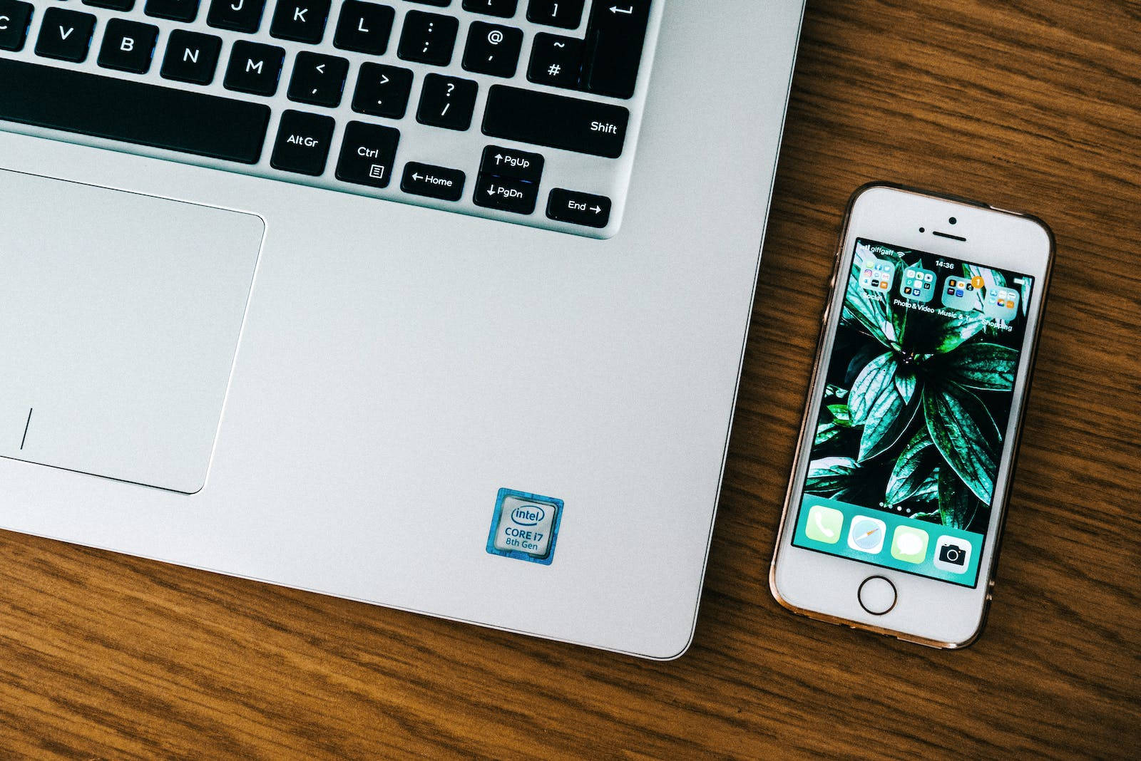 original iPhone 6 桌布 壁紙 — 一台銀色筆記型電腦和一台金色iPhone並排放在溫暖的木桌上，木紋清晰可見。