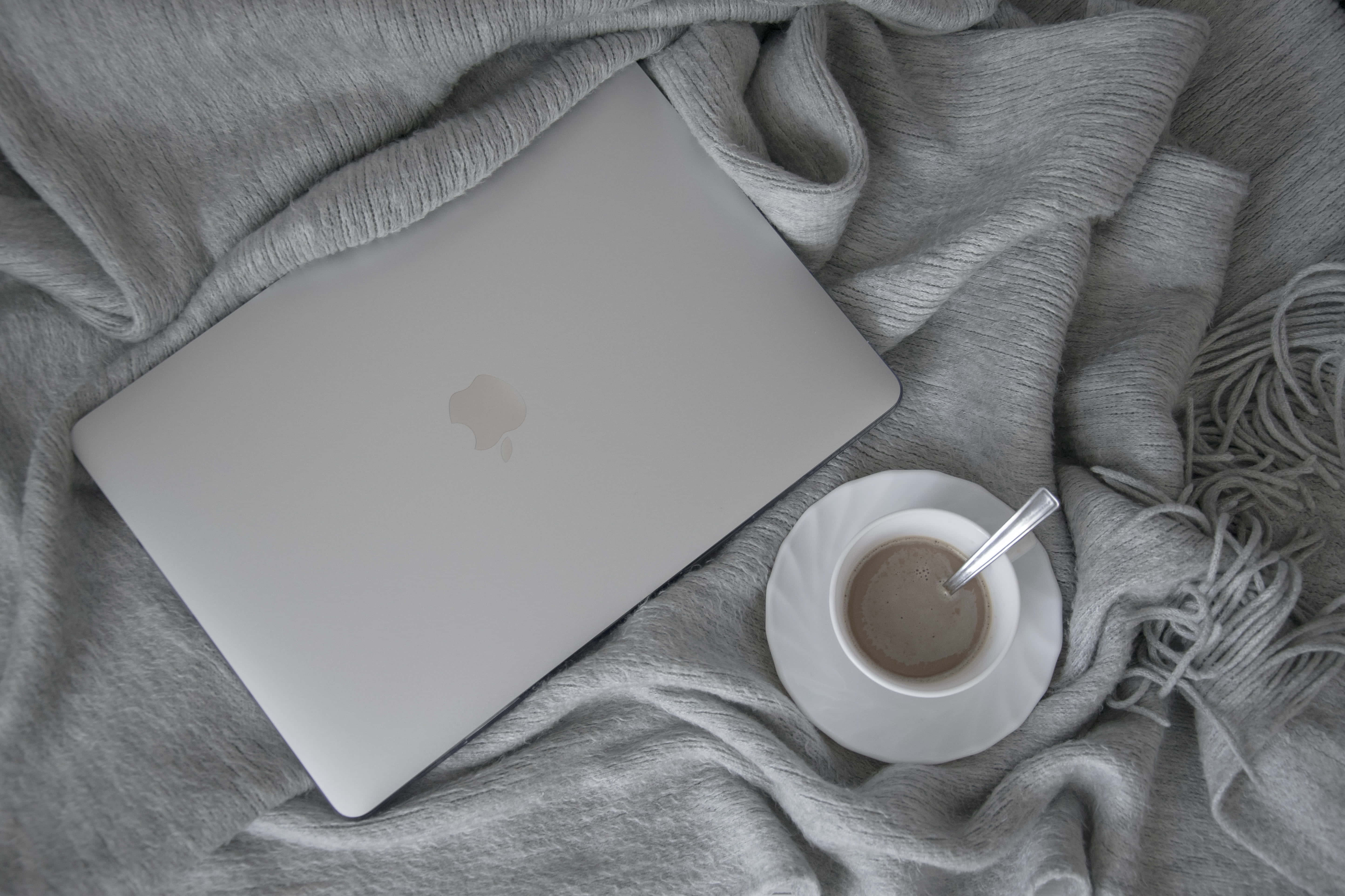 美學 MacBook 壁紙 桌布 壁紙 — 一台銀色筆記型電腦和咖啡杯放在柔軟的灰色毛毯上，營造出舒適簡約的工作空間。