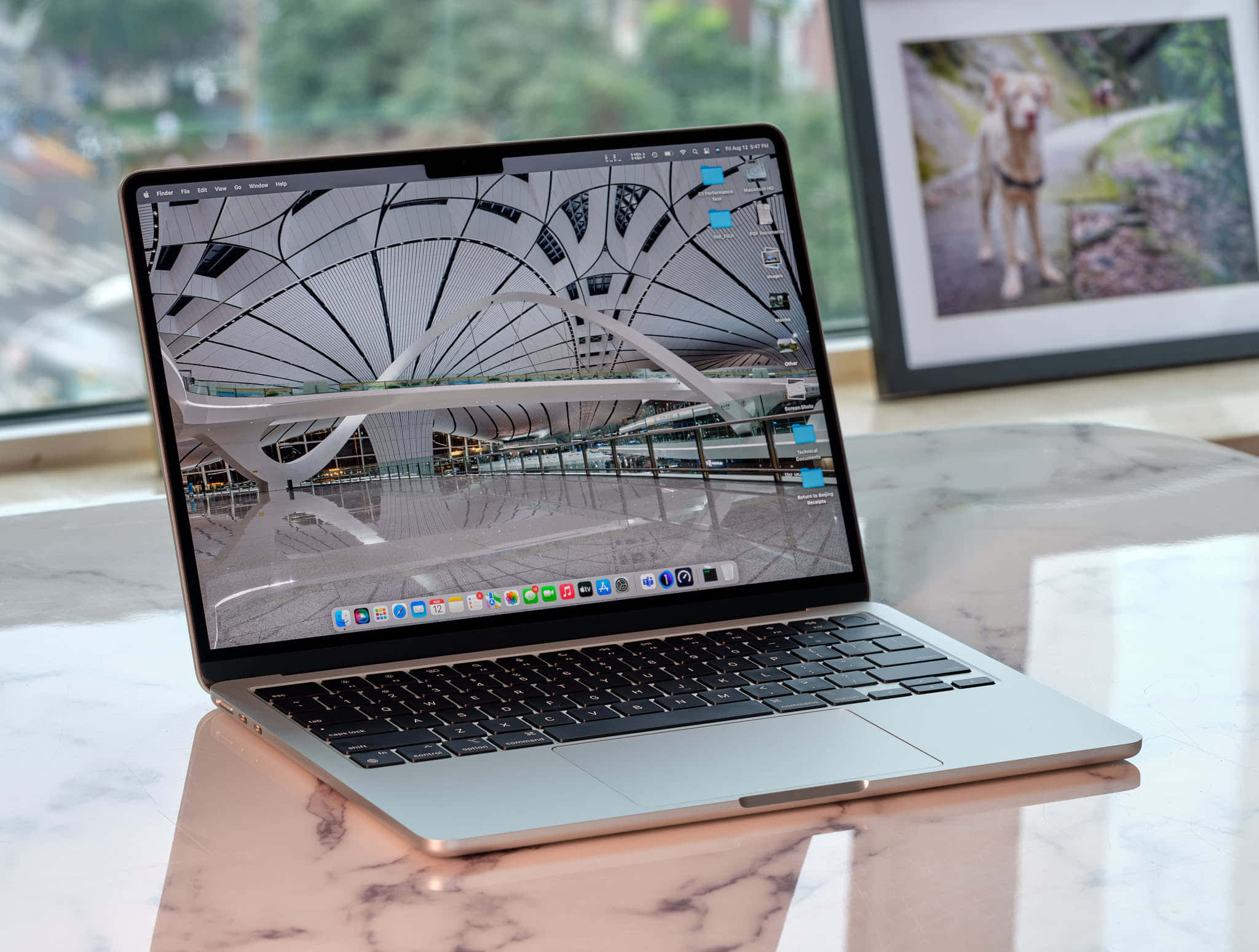 MacBook 動態圖片 桌布 壁紙 — 一台銀色筆記型電腦打開放在大理石桌上，顯示未來主義建築內部，有彎曲的白色橫樑和玻璃欄杆。