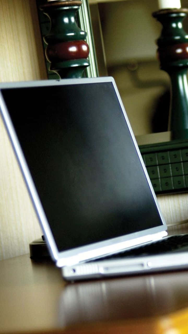 Android Computer 桌布 壁紙 — 一台銀色筆記型電腦搭配黑色螢幕，放在木桌上，旁邊有一個綠色燭台。