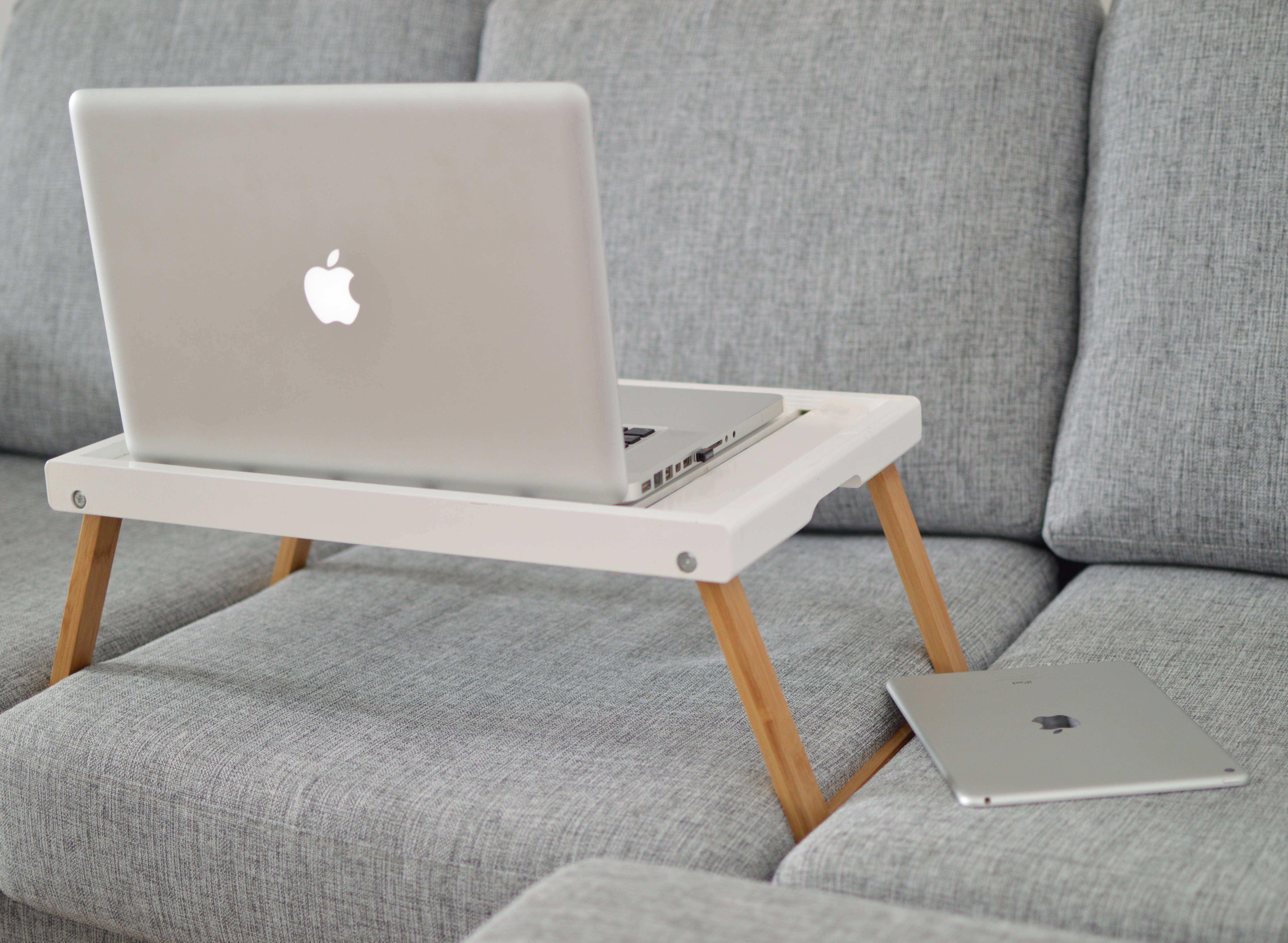 macbook pro 桌布 壁紙 — 一台銀色筆記型電腦放在白色木製膝上桌上，桌子置於灰色布沙發上，旁邊有一台相配的平板電腦。
