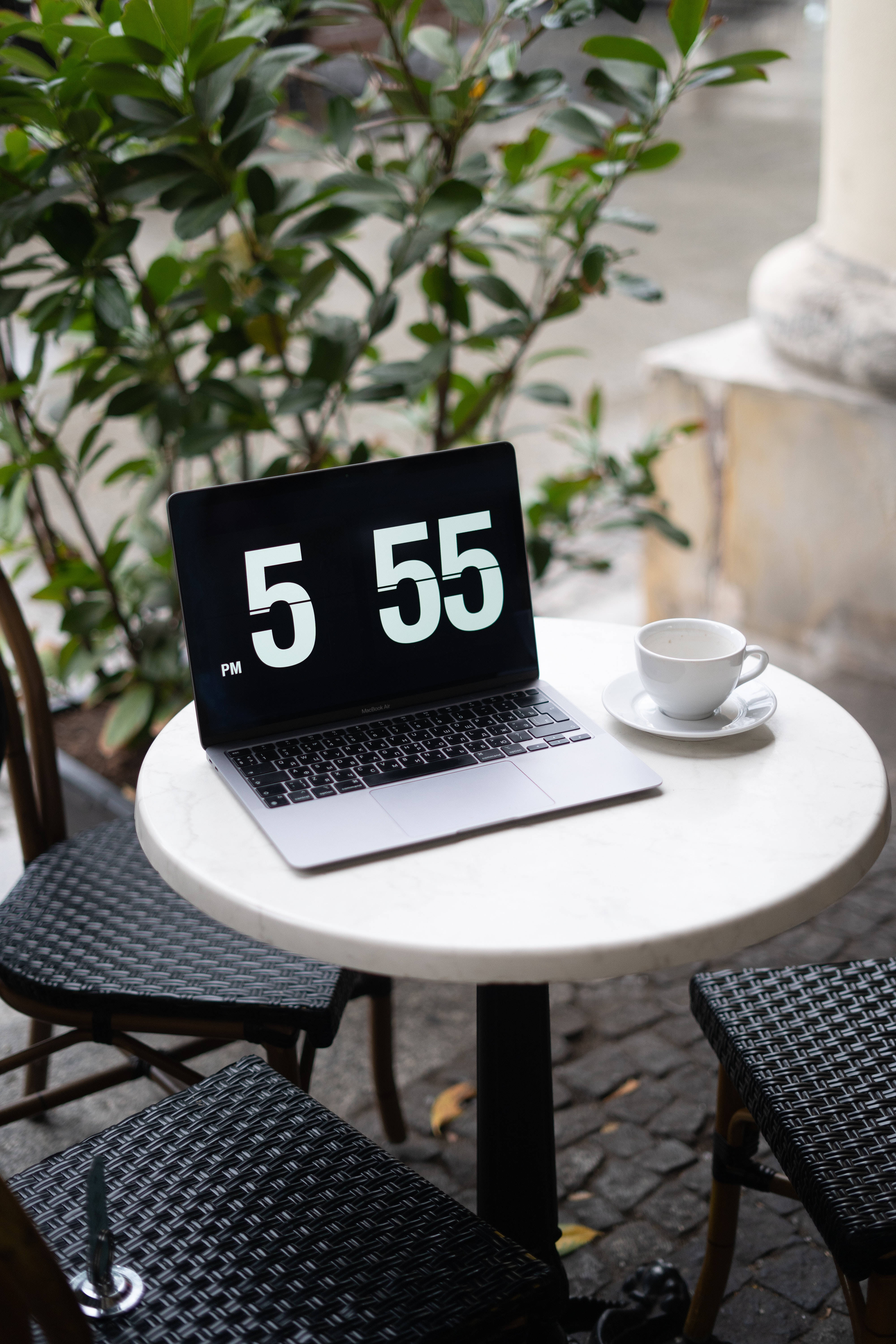 aesthetic tumblr laptop 桌布 壁紙 — 一台銀色筆記型電腦顯示5 55 PM，放在白色大理石咖啡桌上，旁邊有白色咖啡杯，背後有柔焦的綠色植物。