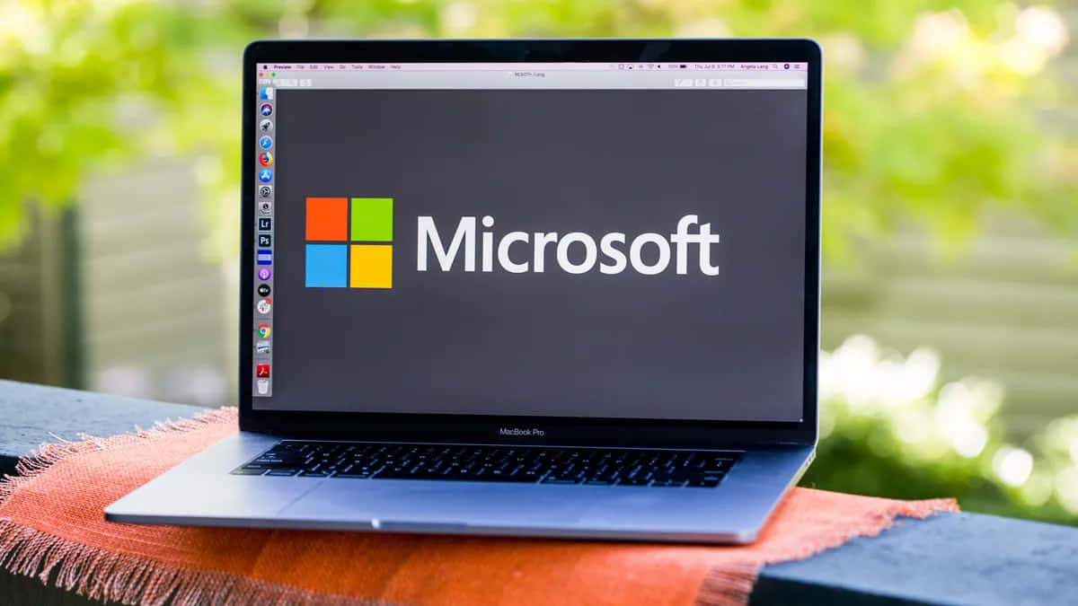 銀色筆記型電腦在螢幕上顯示Microsoft標誌，放在橙色布上戶外。 — Microsoft 壁紙
