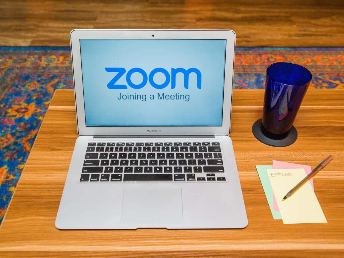 筆記型電腦顯示Zoom加入會議，木桌上有藍色玻璃杯和便利貼。 — 放大 壁紙