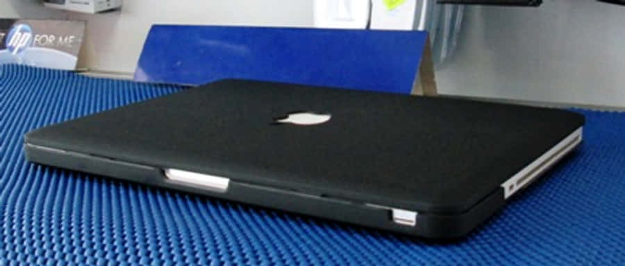Black Macbook 桌布 壁紙 — 一台闔上的黑色筆記型電腦放在有紋理的藍色墊子上，處於簡約的工作空間。