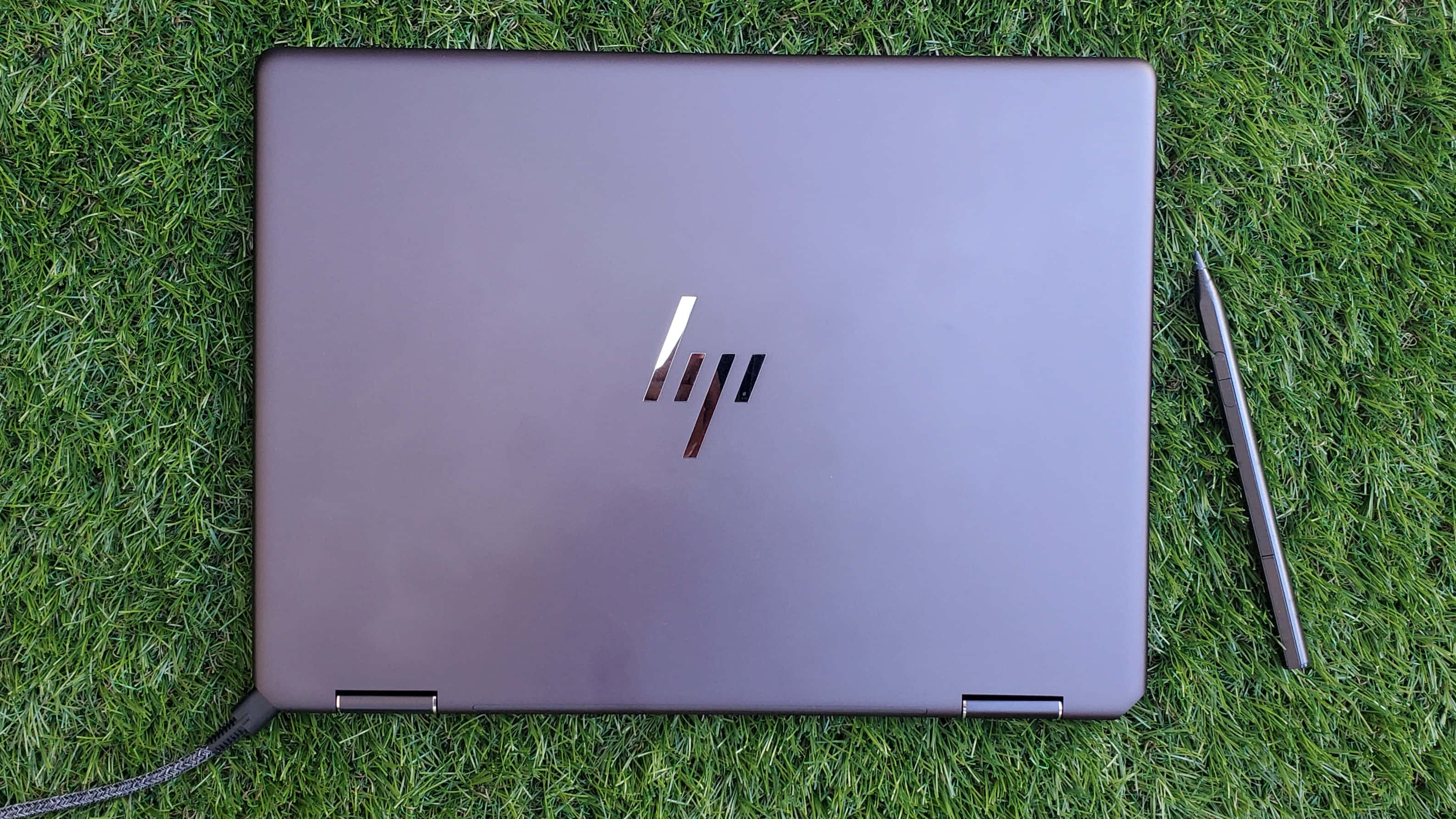 HP 桌布 壁紙 — 一台關閉的銀色 HP 筆記型電腦放在鮮綠色草地上，旁邊有一支觸控筆。