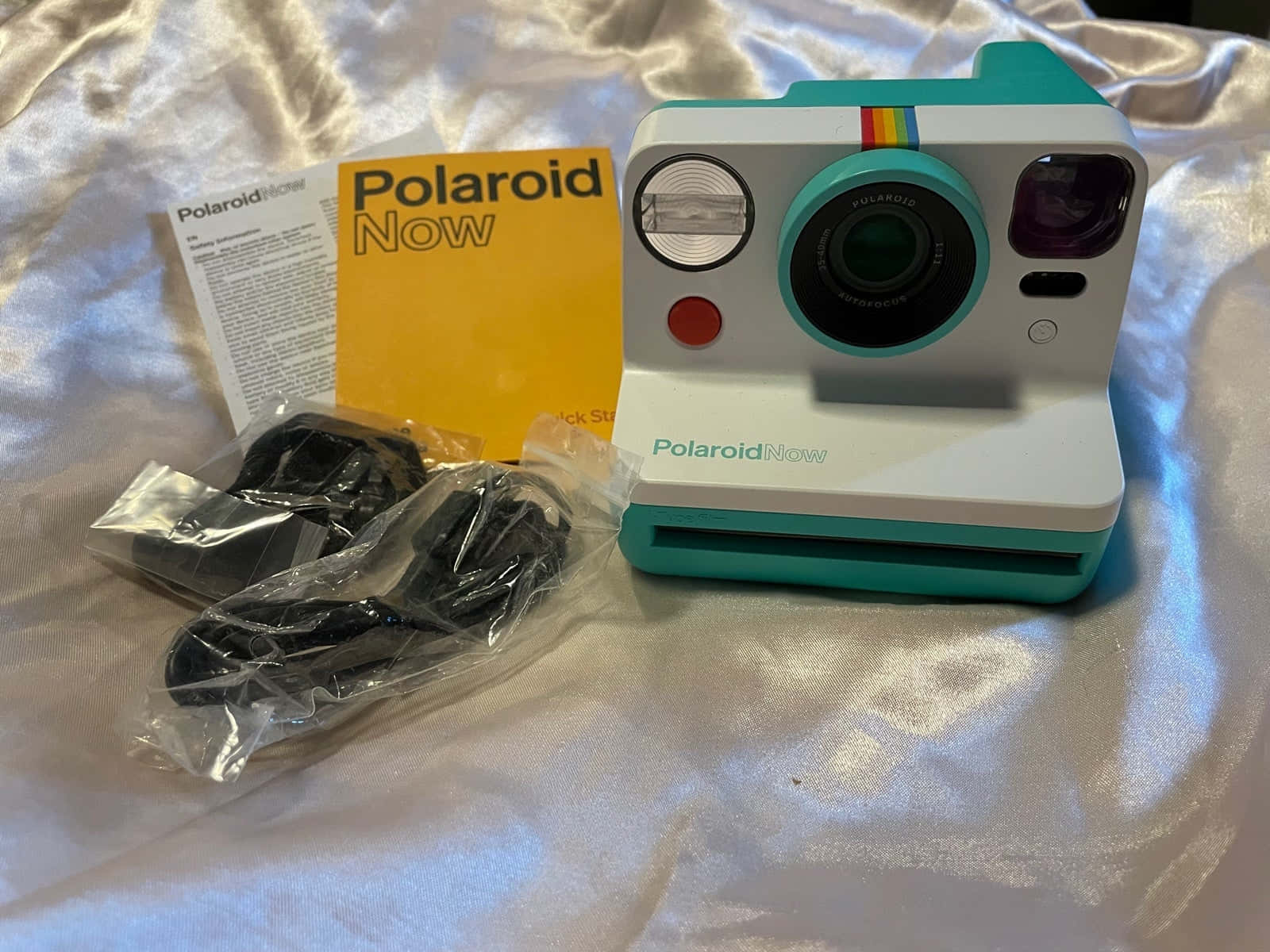 相機 桌布 壁紙 — 一台青綠色和白色的Polaroid Now即時相機連配件，放置在閃亮的銀色緞面表面上。