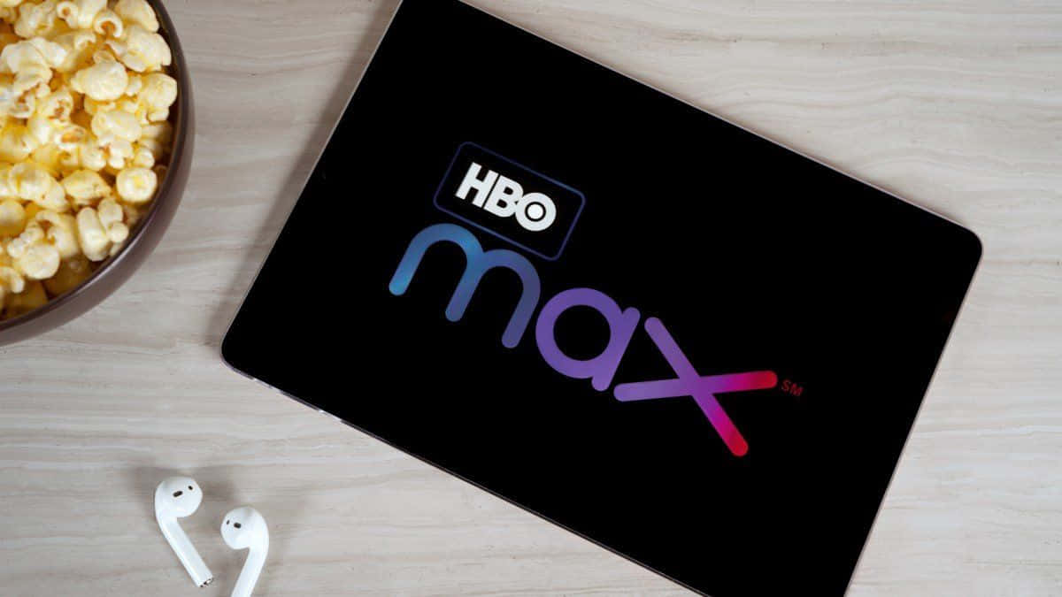 Video-on-demand 桌布 壁紙 — 一台顯示HBO Max標誌的平板電腦，旁邊放著一碗爆米花和白色耳塞，置於淺色木質表面上。
