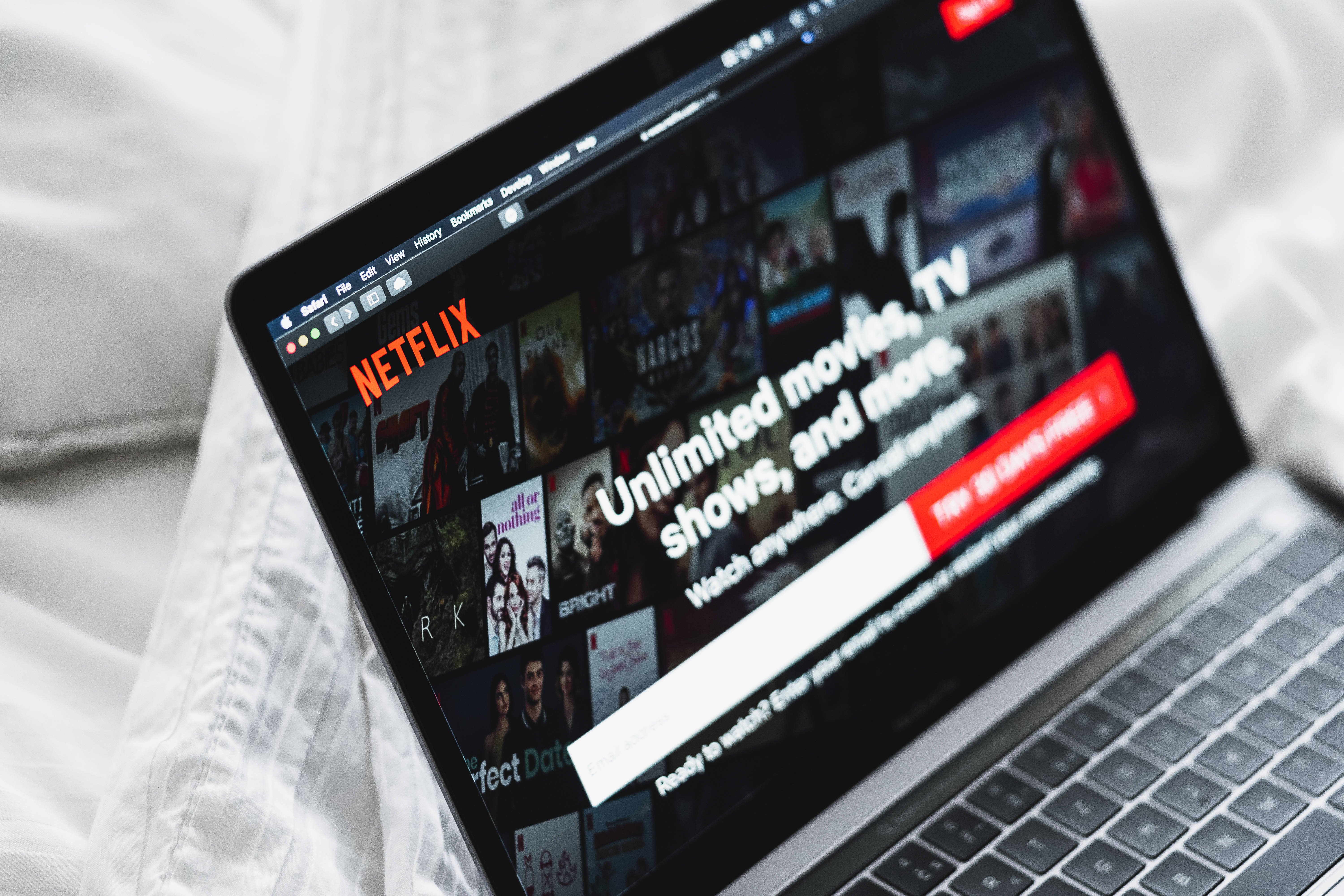 Website 桌布 壁紙 — 一台顯示Netflix首頁的筆記型電腦放在柔軟的白色床單上，營造出舒適的室內氛圍。