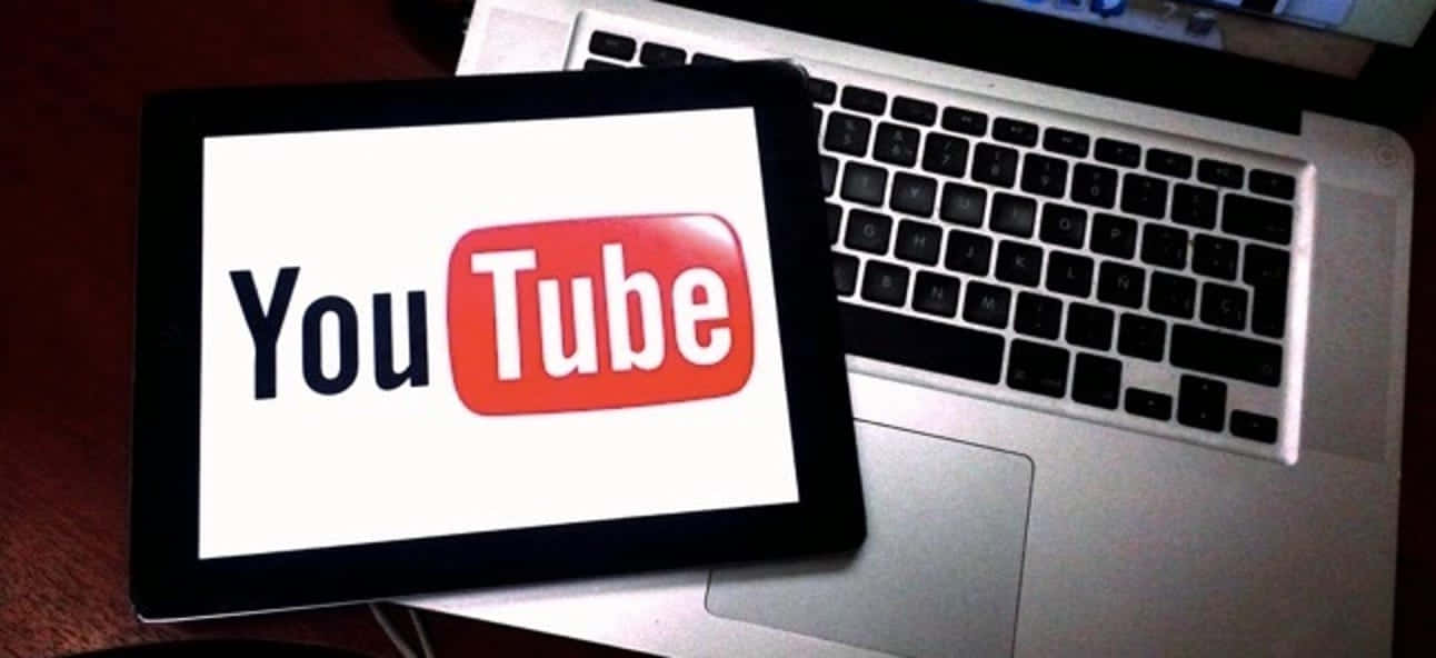 YouTube 桌布 壁紙 — 一台顯示YouTube標誌的平板電腦放在木桌上的一部銀色筆記型電腦鍵盤上。