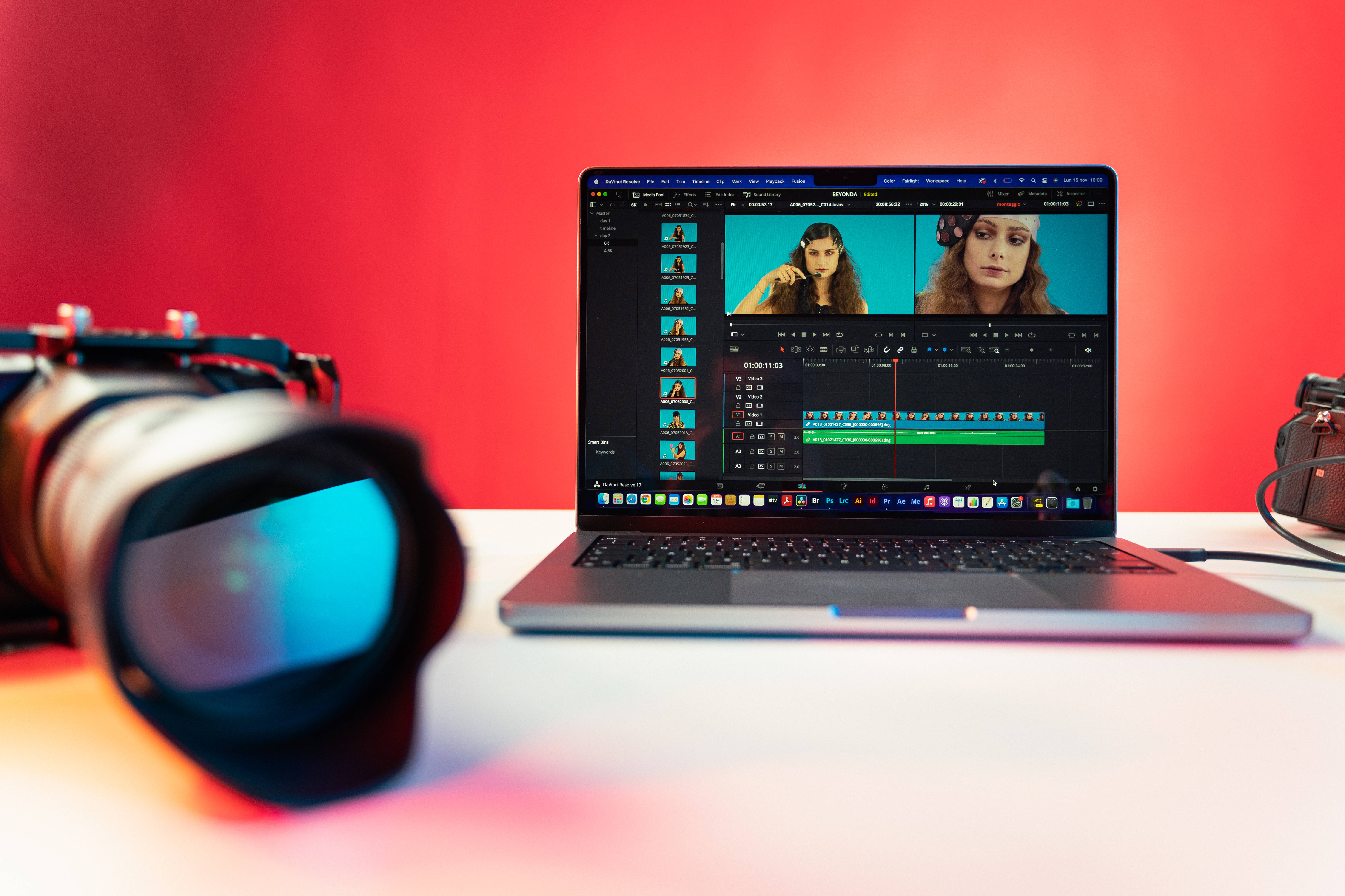 Editing 桌布 壁紙 — 一台顯示影片編輯軟體的筆記型電腦放在白色桌子上，旁邊有一個大型相機鏡頭和一台復古相機，背景是鮮紅色的牆壁。