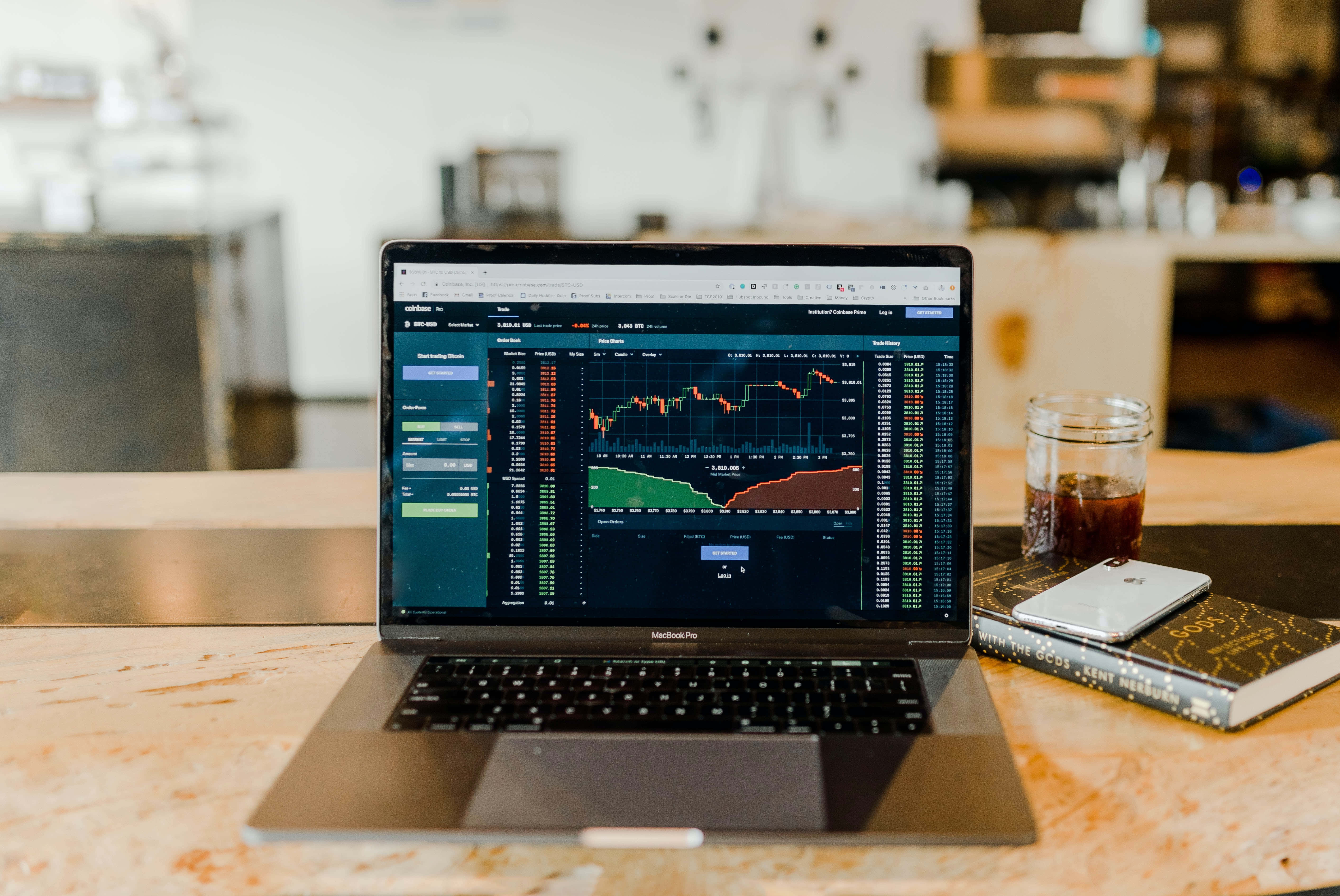 Trading 桌布 壁紙 — 一台顯示財務圖表的筆記型電腦放在現代咖啡館的大理石檯面上，旁邊有一杯咖啡和一本書。