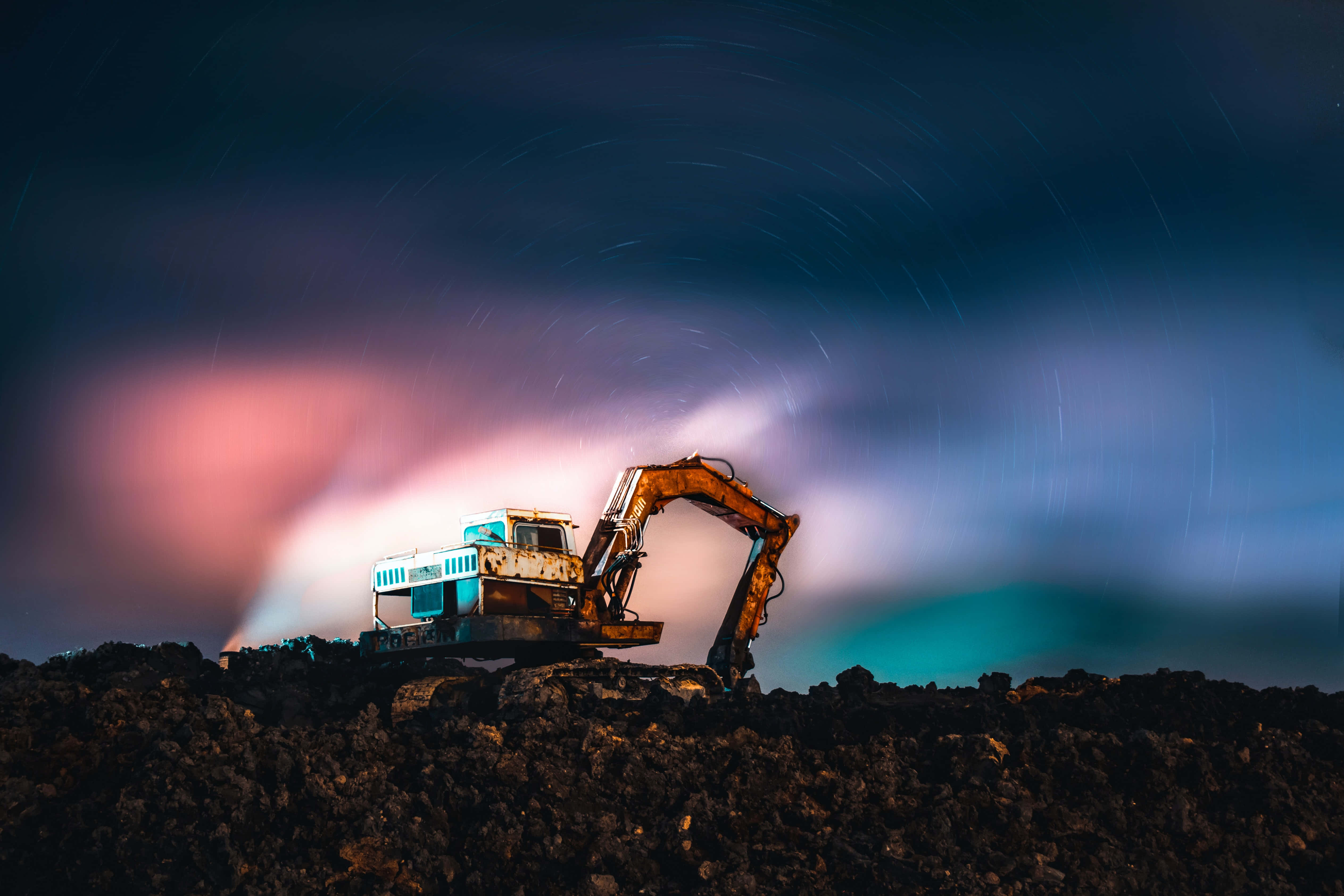 Mining 桌布 壁紙 — 一台風化的挖掘機矗立在岩石山丘上，天空中有粉紅色和藍綠色的極光色調的星軌。