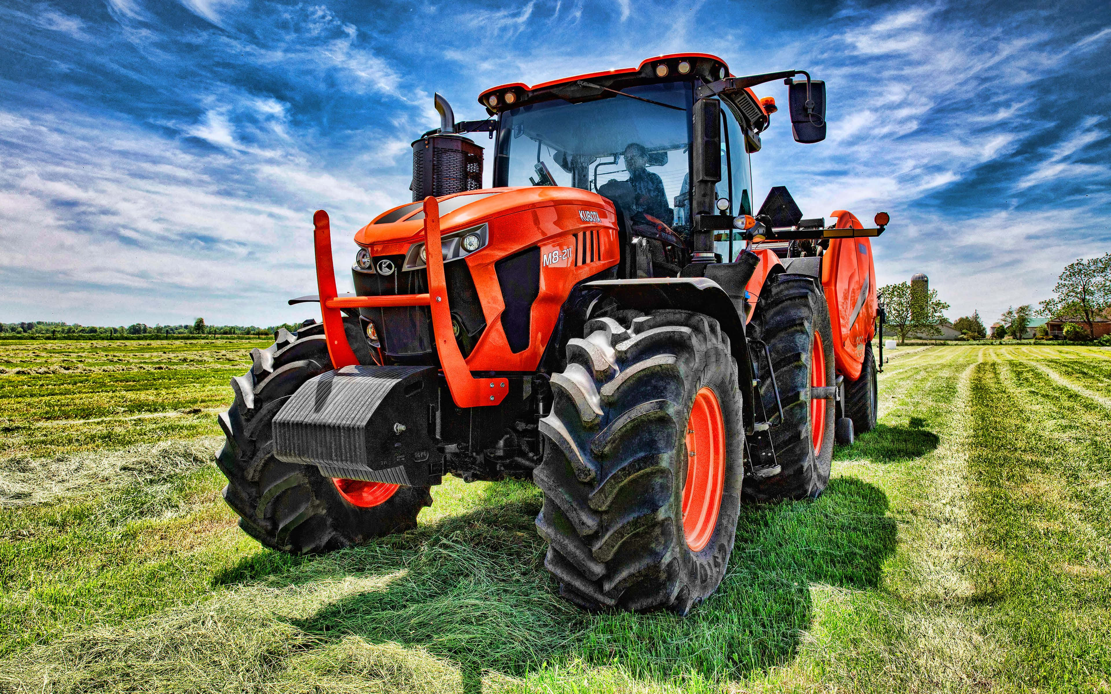 Tractor 桌布 壁紙 — 一台鮮橘色拖拉機配備大型黑色輪胎，停在新割的綠色田野中，背景是帶有縷縷白雲的戲劇性藍天。