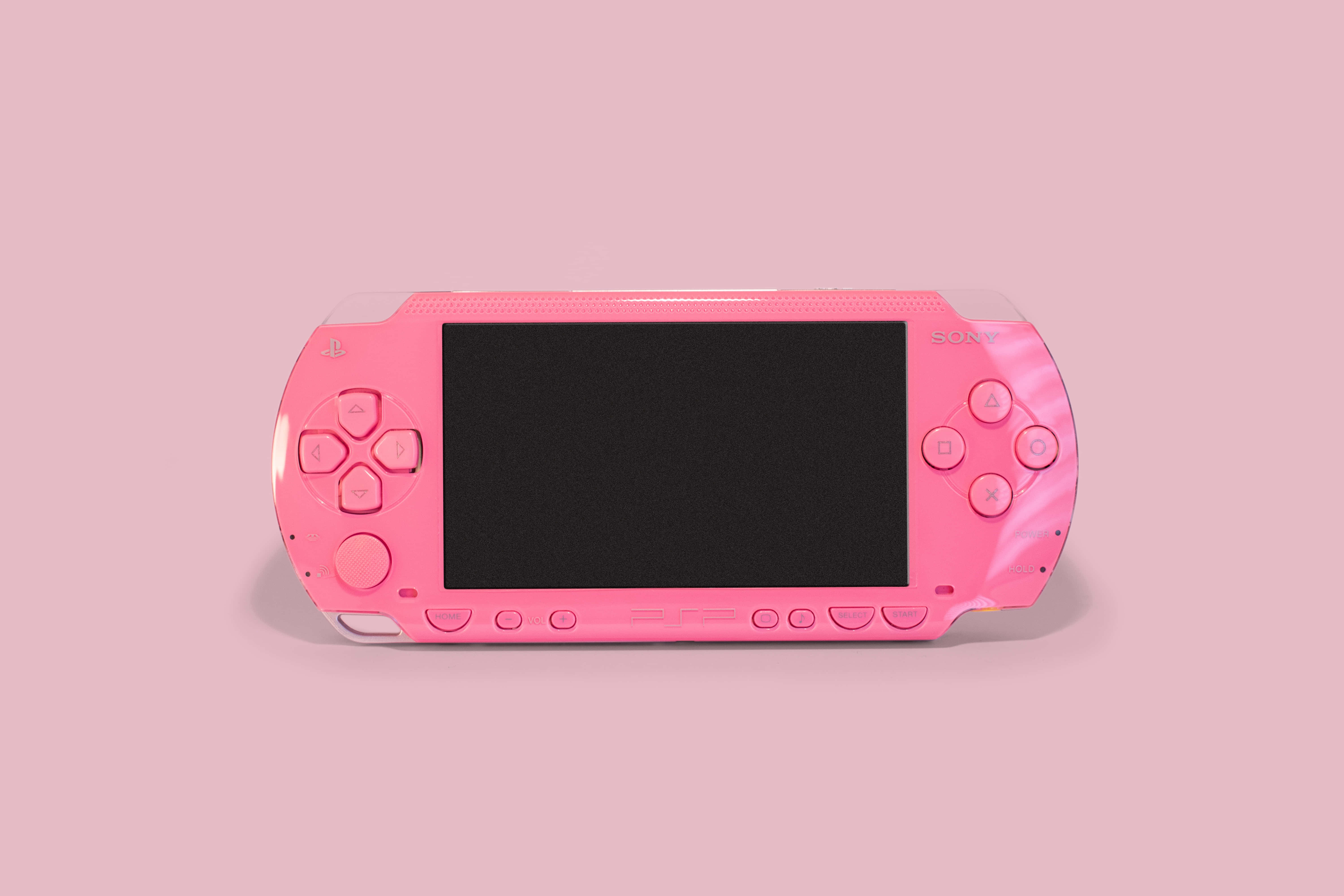 Gaming Consoles 桌布 壁紙 — 一台鮮粉紅色的 Sony PlayStation Portable 主機，置於柔和粉紅背景中央，搭配乾淨的攝影棚燈光。