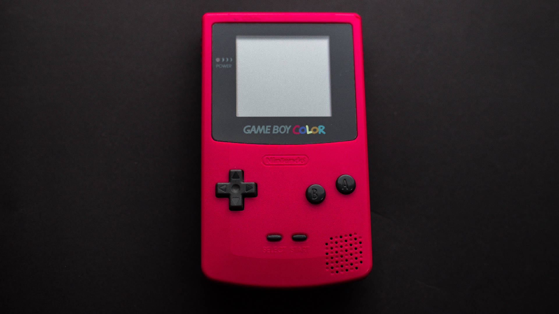 game 桌布 壁紙 — 一台鮮粉紅色的Game Boy Color置於純黑背景中央，螢幕關閉，按鈕正等待遊戲。