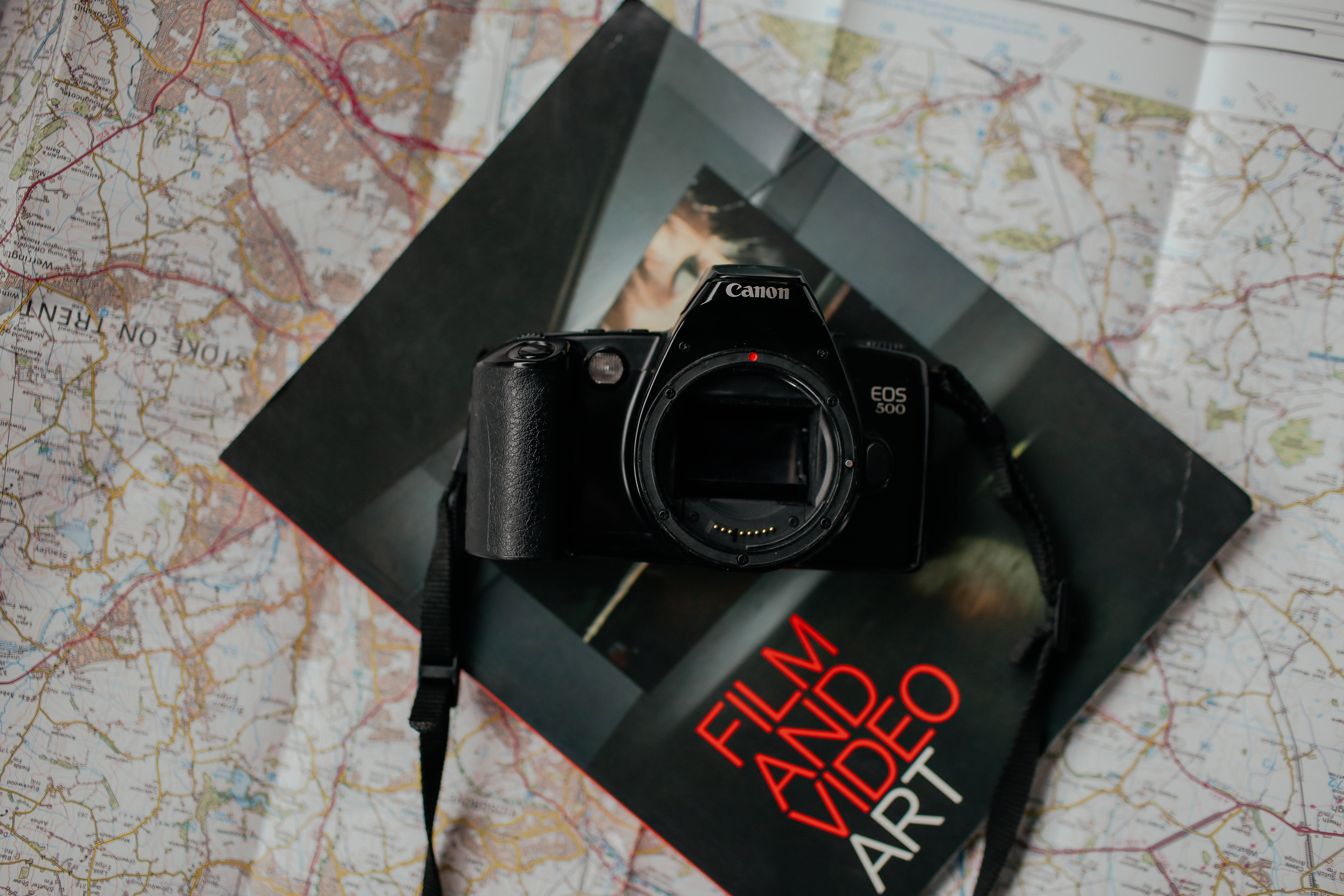 雜誌 桌布 壁紙 — 一台黑色 Canon EOS 300 DSLR 相機放在一本名為 'Film Video Art' 的書上，書本置於詳細的道路地圖上。