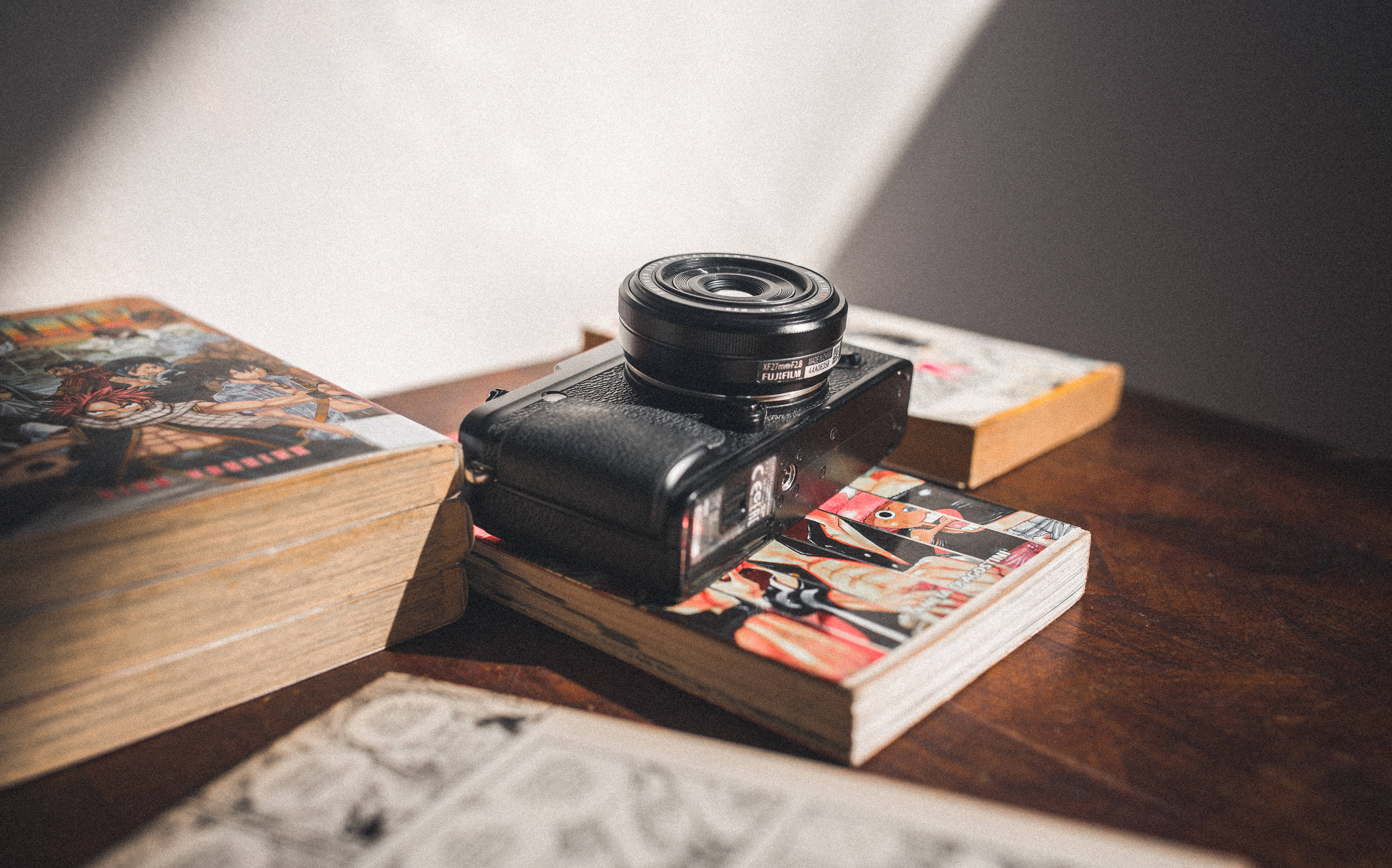 Retro Aesthetic 桌布 壁紙 — 一台黑色 Fujifilm 相機放在色彩繽紛的漫畫書上，沐浴在溫暖的陽光下，置於木桌上。