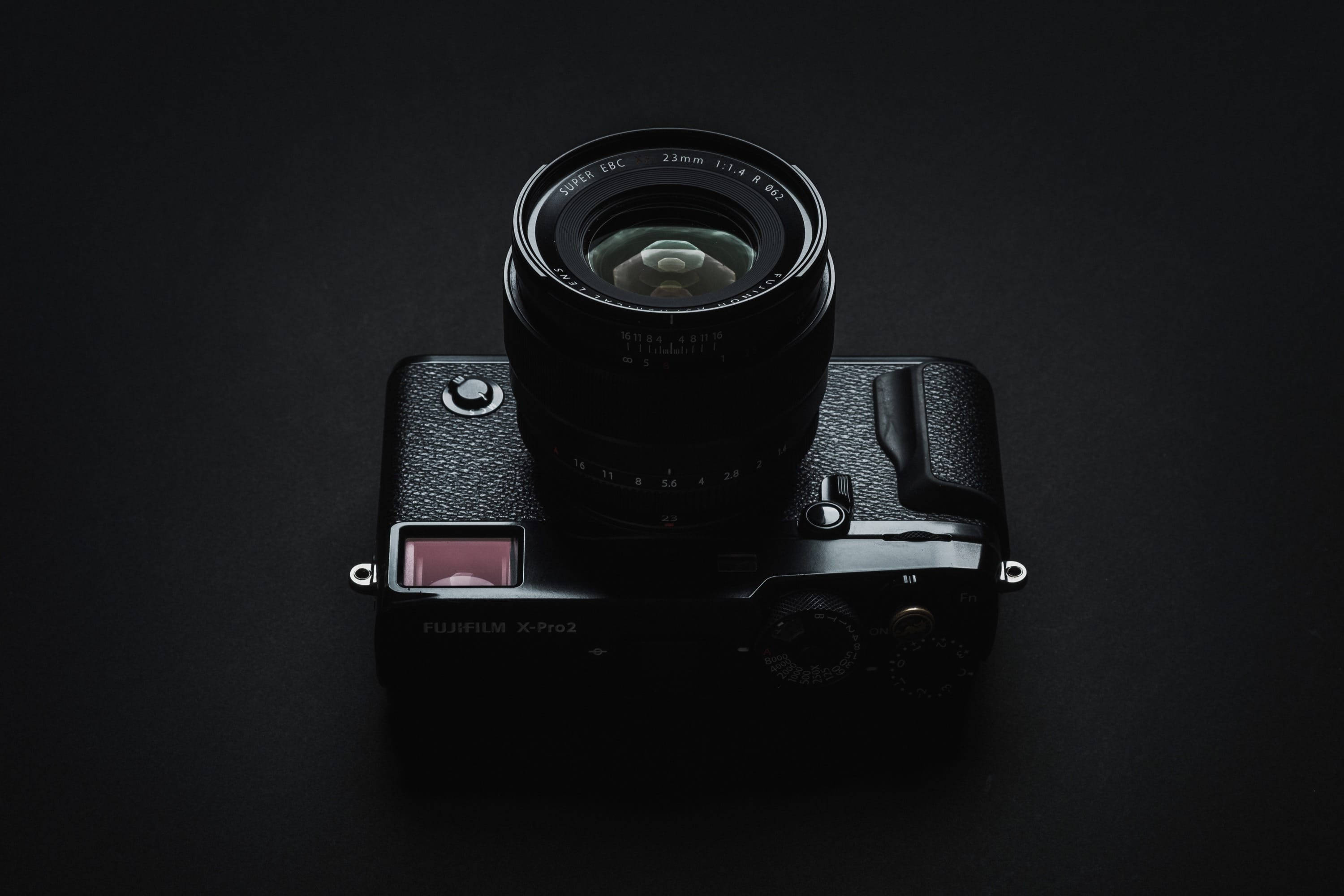 相機 桌布 壁紙 — 一台黑色Fujifilm X-Pro2相機配備23mm鏡頭，置於深色背景中央，從上方打光以突顯其紋理機身和金屬轉盤。