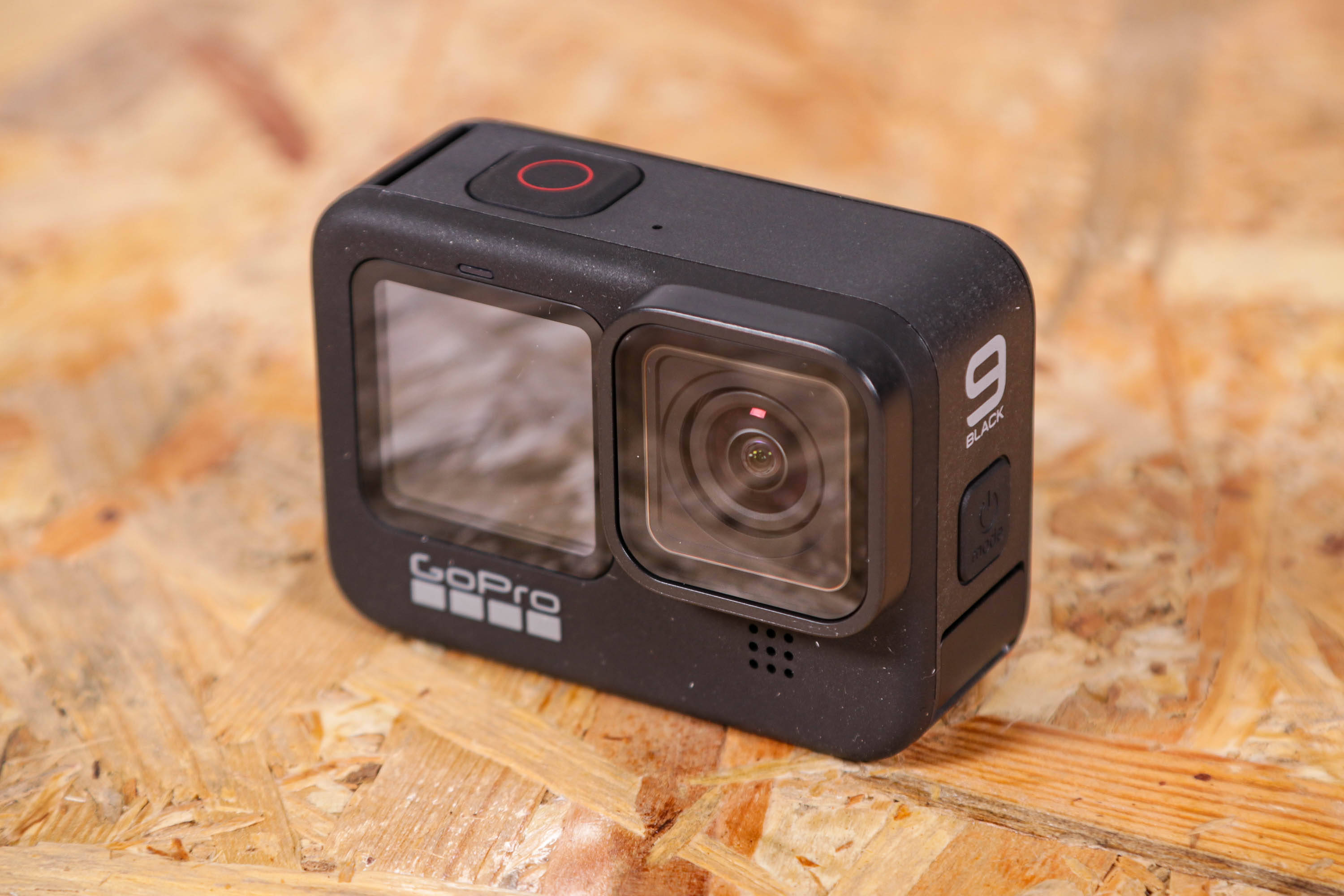 攝影 桌布 壁紙 — 一台黑色GoPro 9 Black運動相機放置在帶有天然木紋的紋理膠合板表面上。