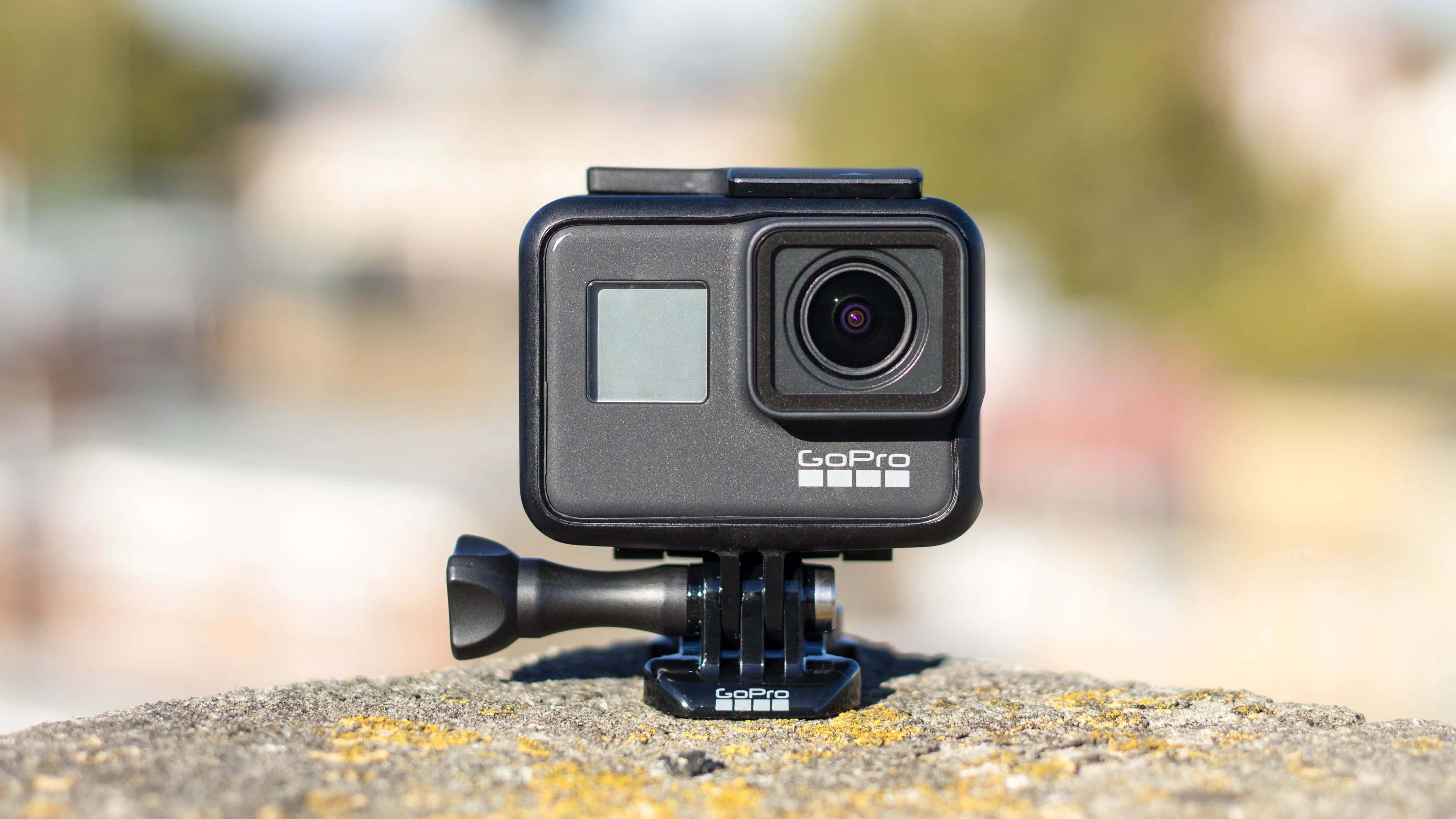 gopro 桌布 壁紙 — 一台黑色GoPro相機安裝在岩石表面上，背景為模糊的戶外景色。