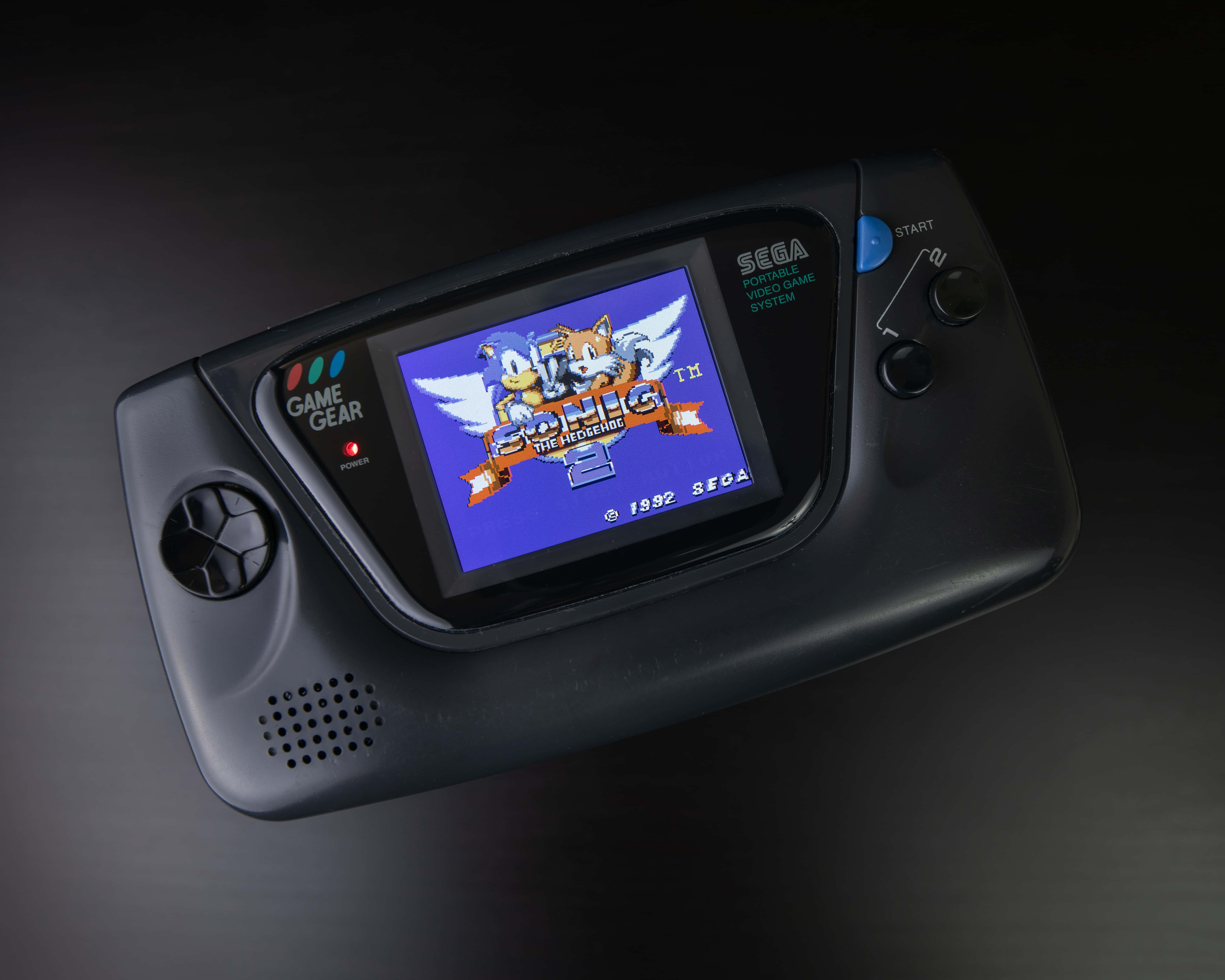 Gaming Consoles 桌布 壁紙 — 一台黑色Sega Game Gear掌上遊戲機在深色反光表面上顯示Sonic the Hedgehog 2的標題畫面。