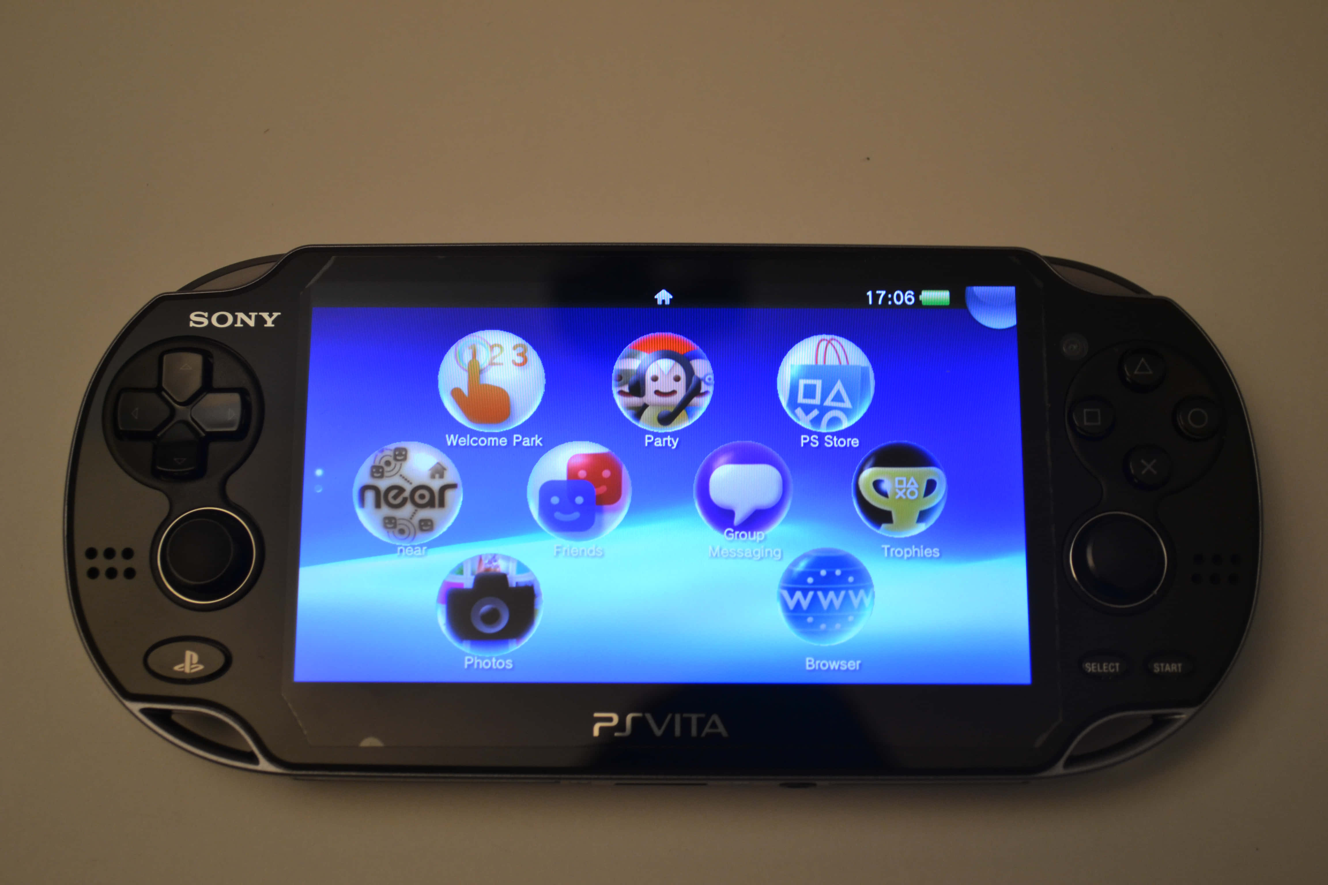 PlayStation 桌布 壁紙 — 一台黑色Sony PS Vita掌上型遊戲機在藍色漸層背景上顯示其主畫面，帶有色彩繽紛的應用程式圖示。