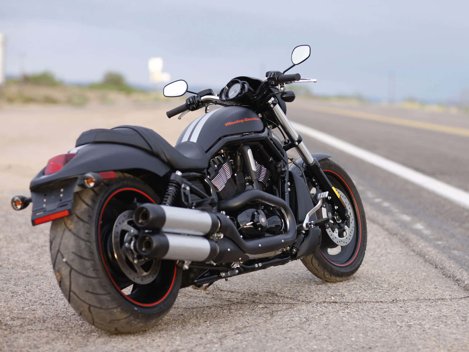 Harley Davidson HD 桌布 壁紙 — 一台黑色哈雷機車帶有紅色點綴，停在陰天下空無一人的柏油路上。