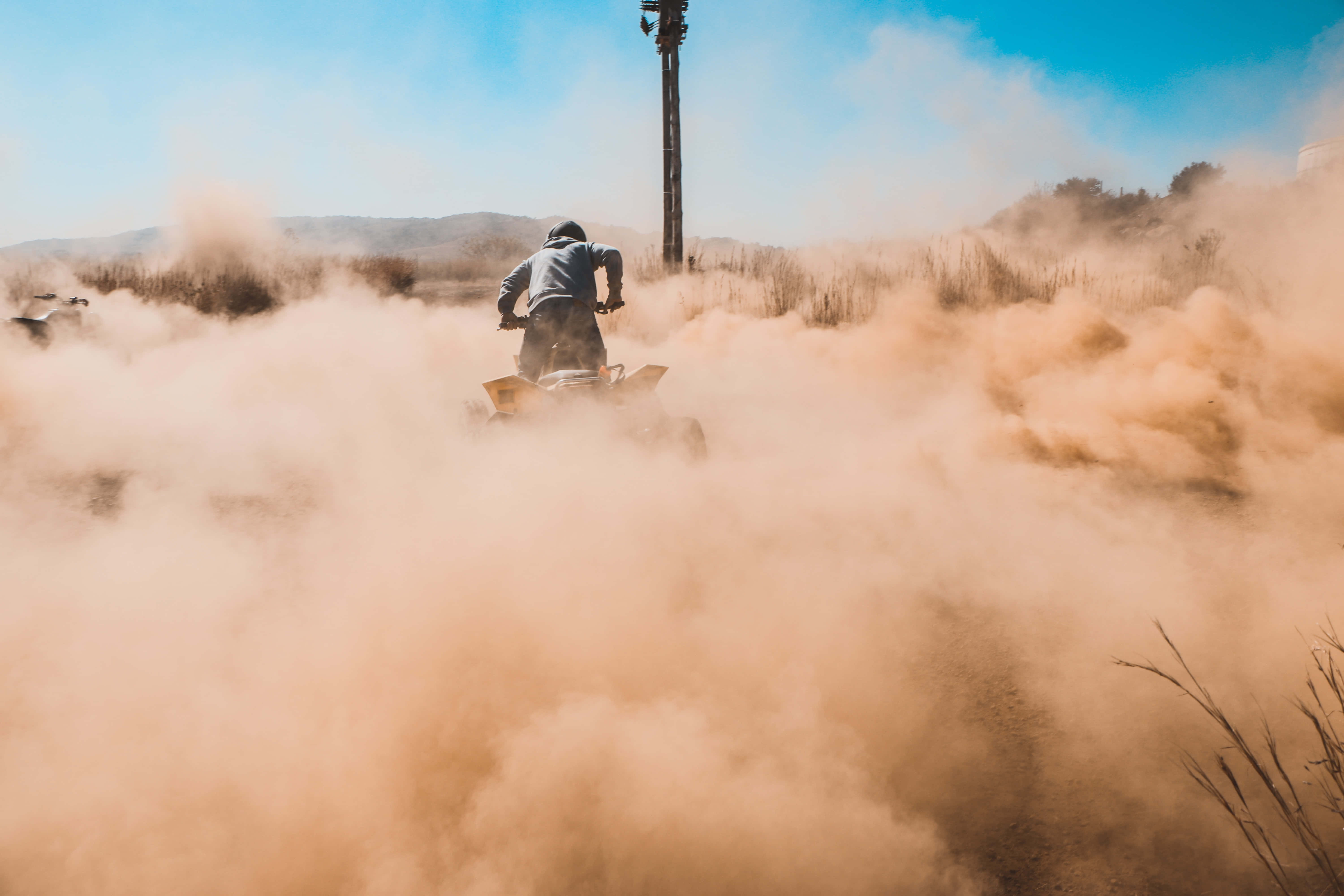 Dust 桌布 壁紙 — 一名ATV騎士在晴朗的藍天下，在乾燥的草地上揚起巨大的橙色塵雲。