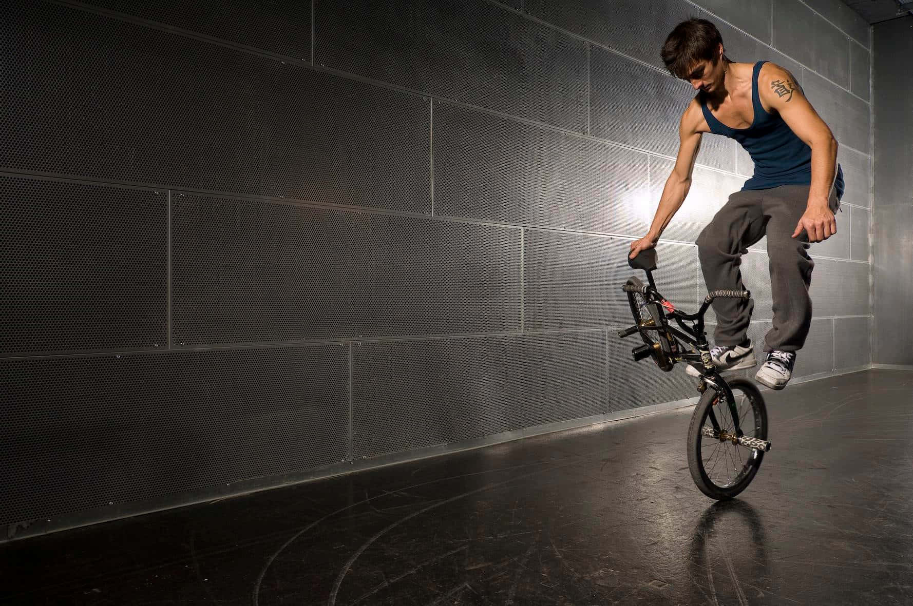 bmx 桌布 壁紙 — 一名BMX車手在昏暗的室內空間對著深色穿孔牆壁表演翹孤輪。