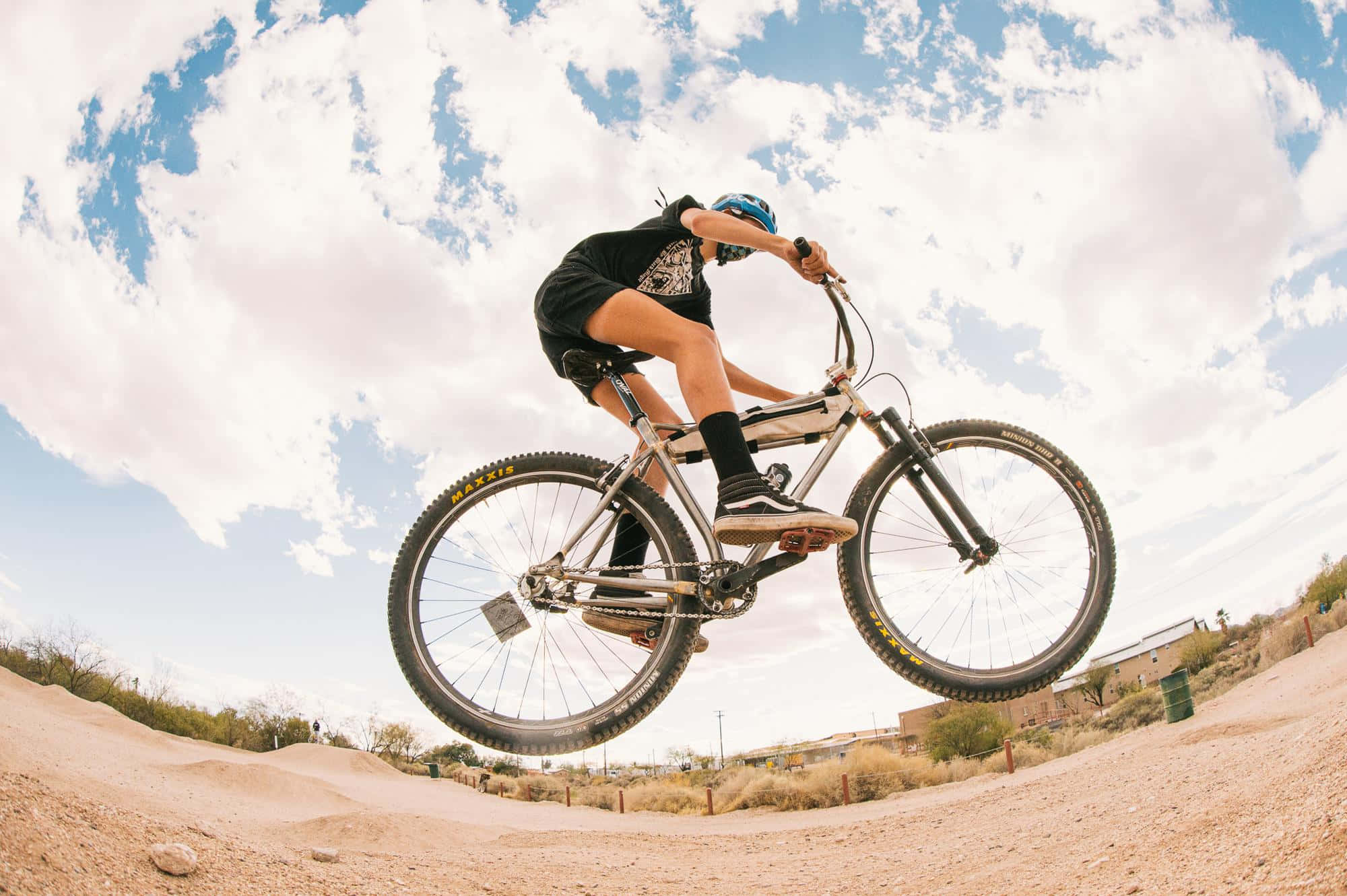 bmx 桌布 壁紙 — 一名BMX車手在晴朗多雲的天空下，飛越塵土飛揚的沙漠小徑。