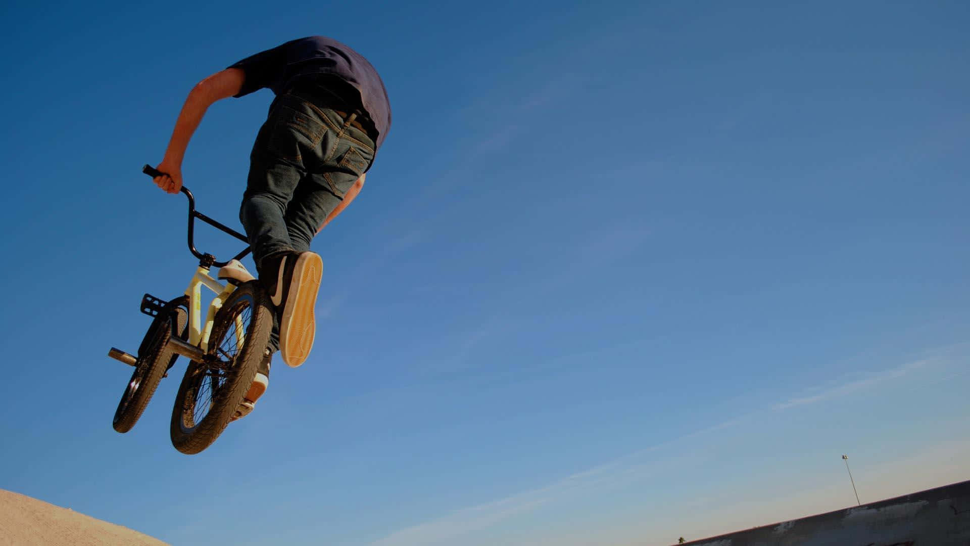 bmx 桌布 壁紙 — 一名bmx車手在清澈的藍天下，於混凝土坡道上空飛翔，表演大膽的特技。