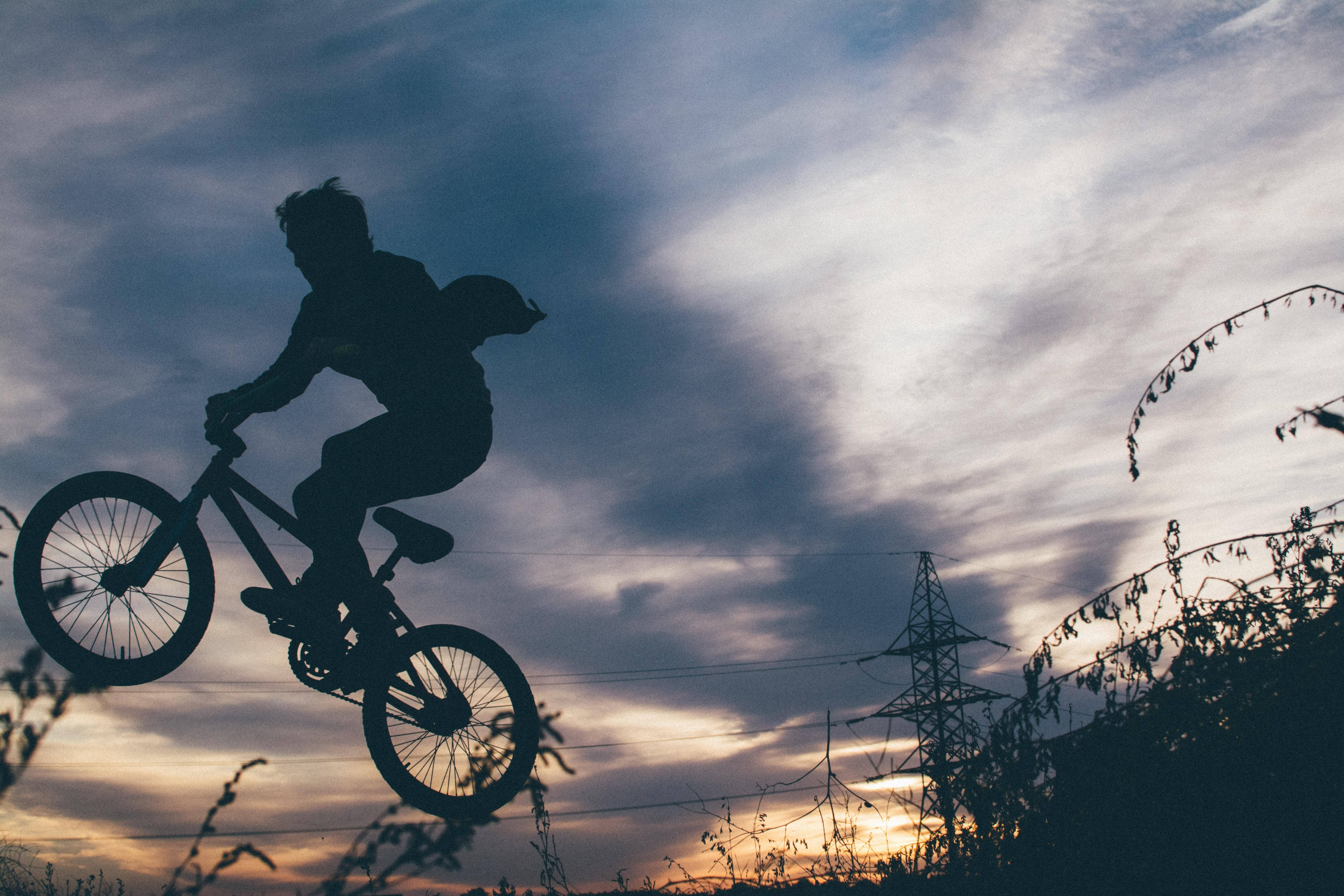bike riding 桌布 壁紙 — 一名BMX車手在空中剪影，背景是戲劇性的日落天空，下方有電線和樹葉。