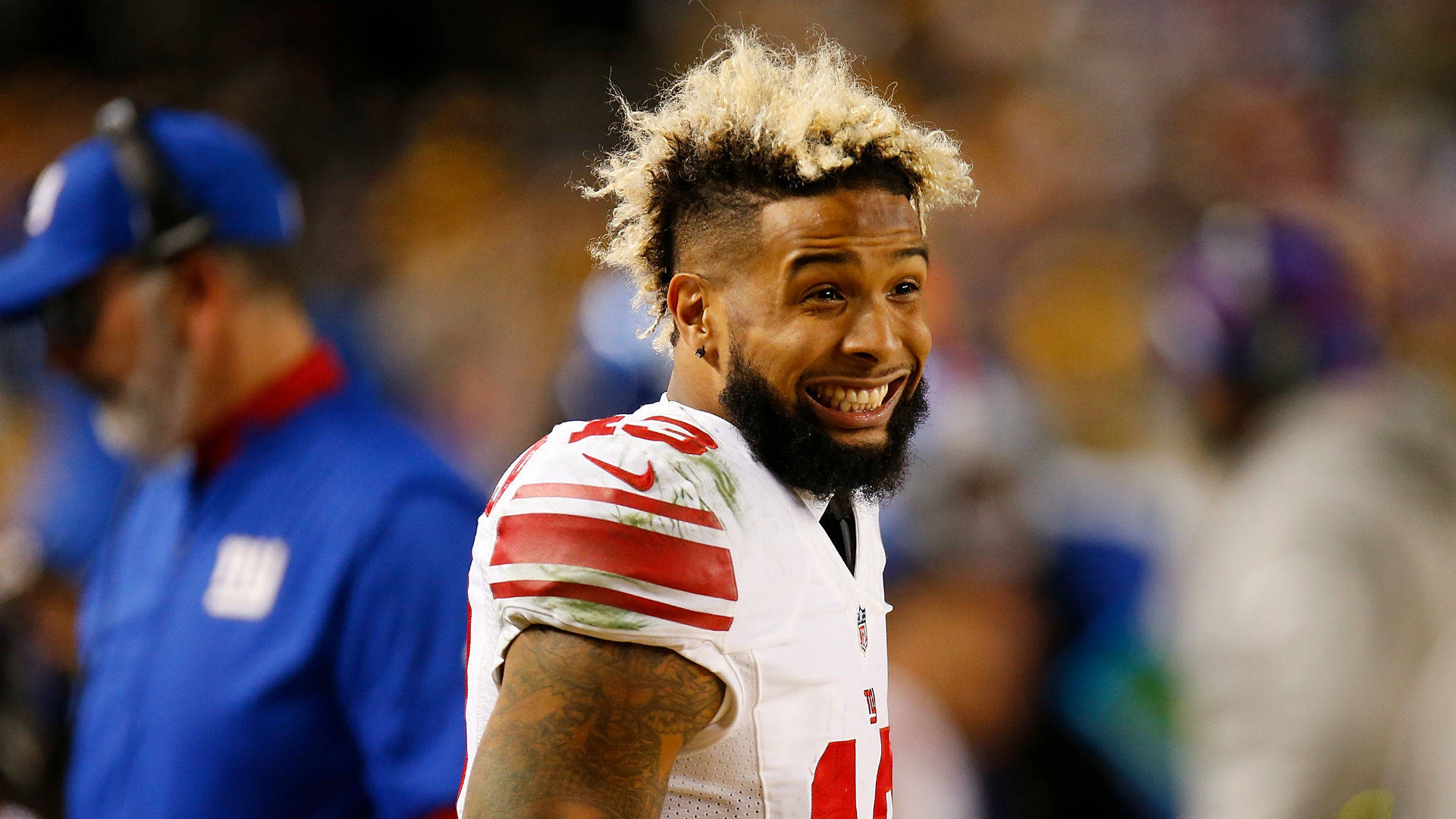 Odell 桌布 壁紙 — 一名NFL球員微笑，漂白頭髮和鬍鬚，身穿白色帶紅色條紋球衣，在比賽中看向鏡頭外。