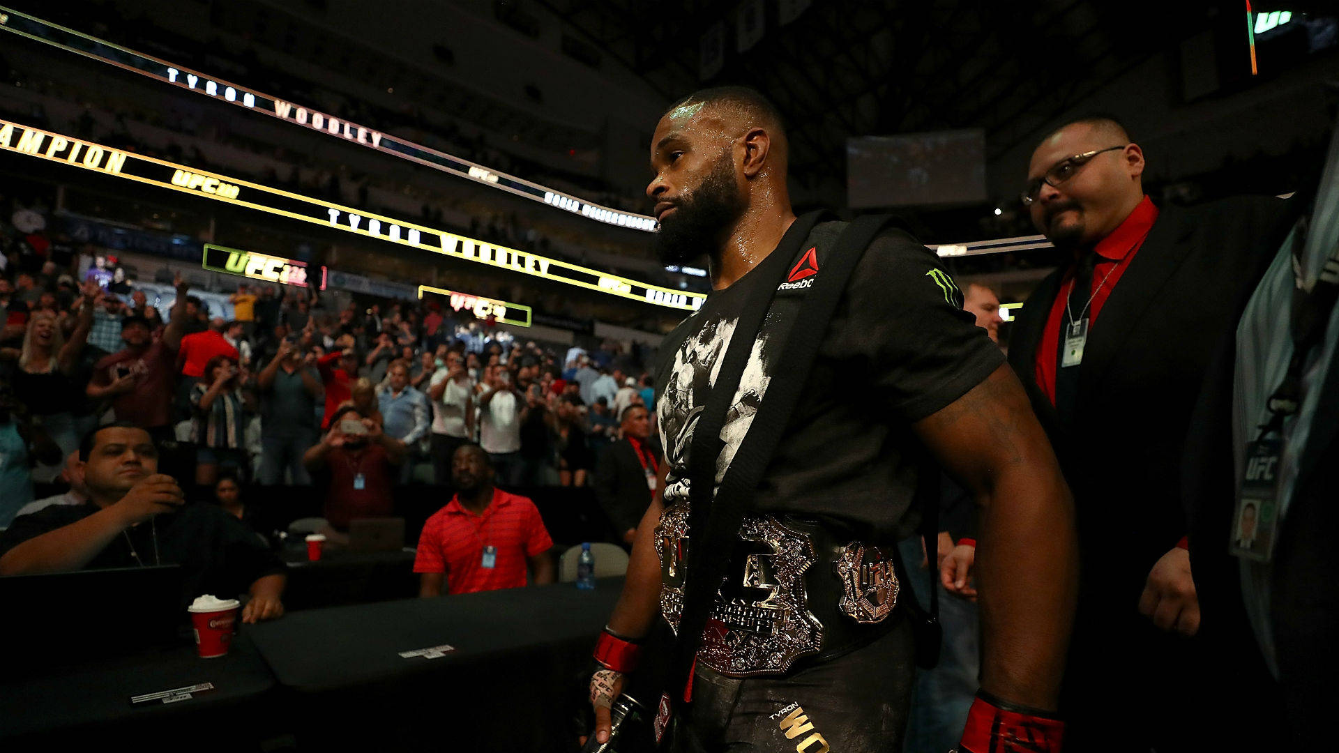 Tyron Woodley 桌布 壁紙 — 一名UFC拳手戴著冠軍腰帶，在明亮的燈光下穿過競技場的人群。